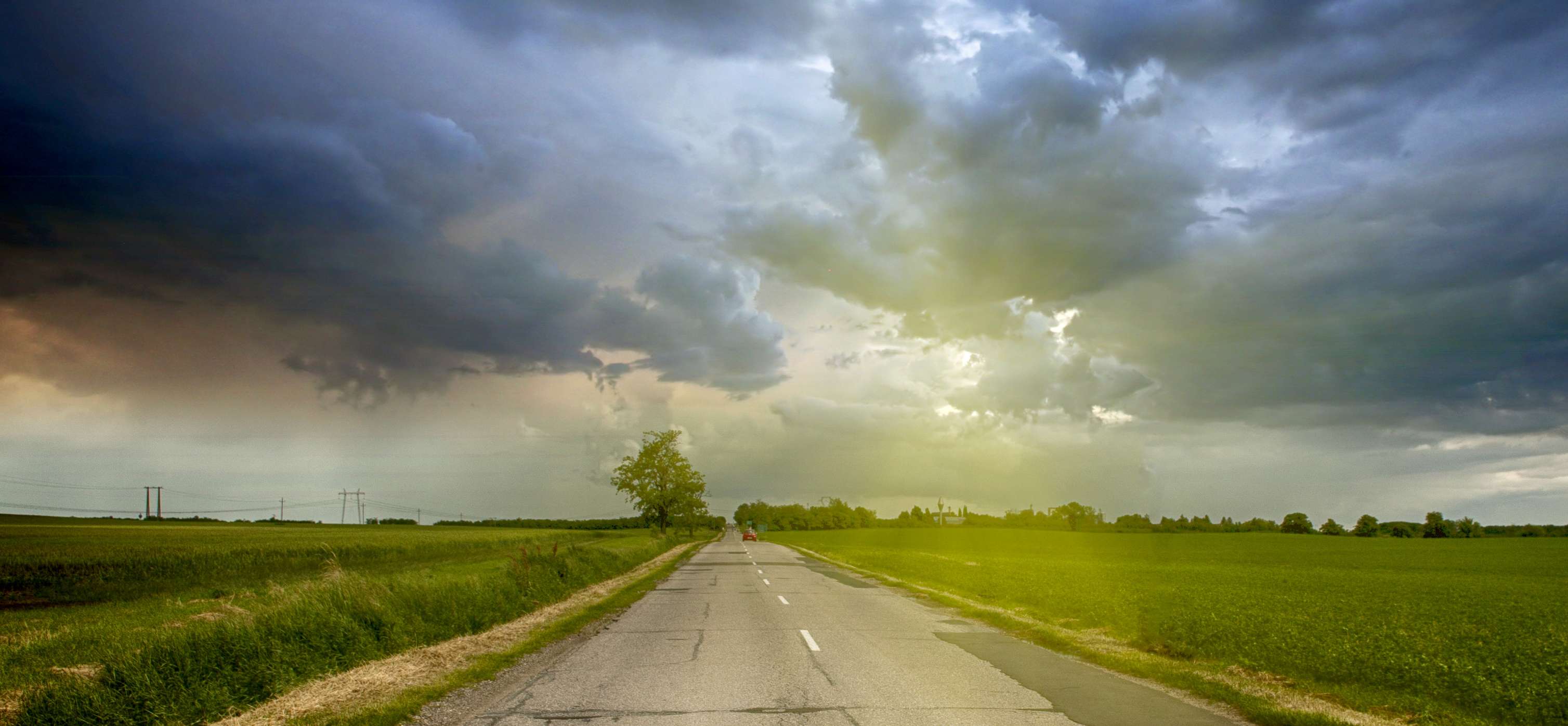 Allianz Unwetterschäden vorbeugen: Eine leere Straße führt durch Felder unter dunklen Wolken