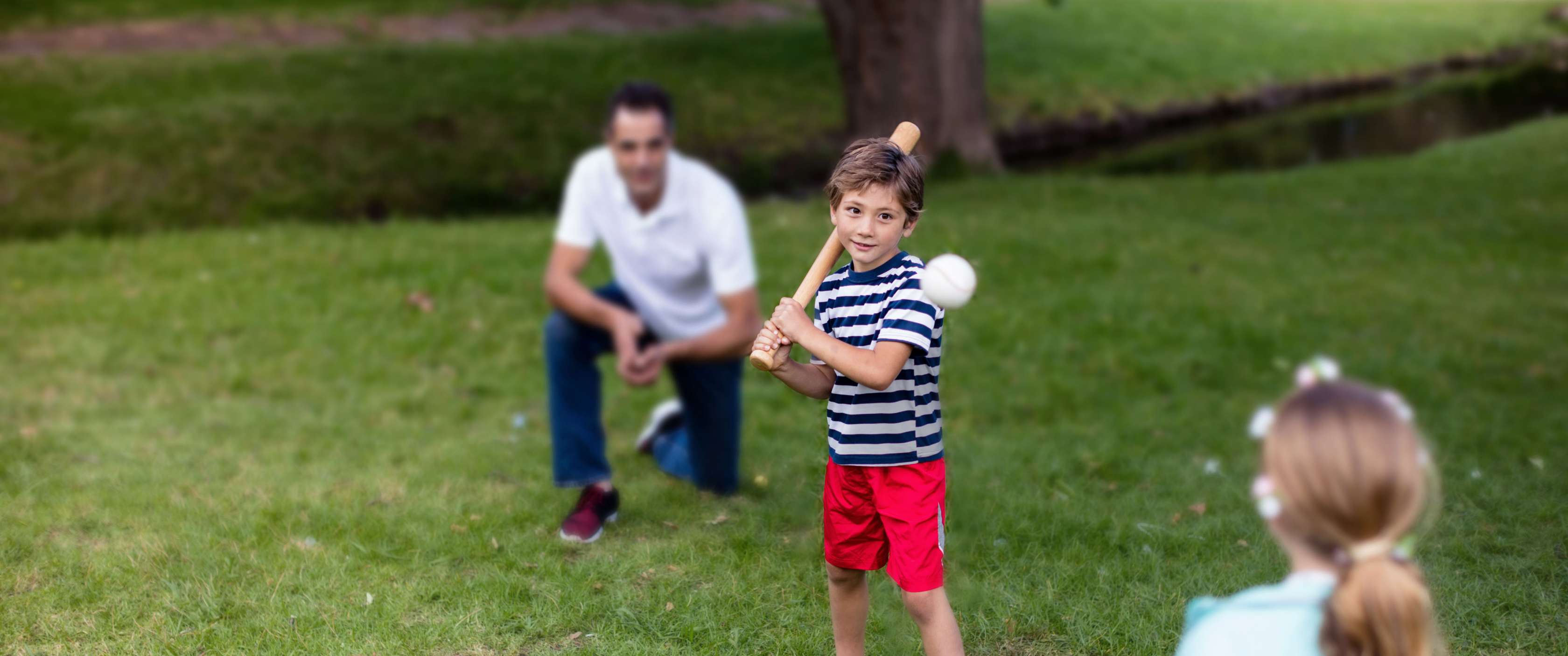 Familienversicherung: Kleiner Junge schlägt nach einem fliegenden Baseball, während der Vater als Fänger hinter ihm kniet