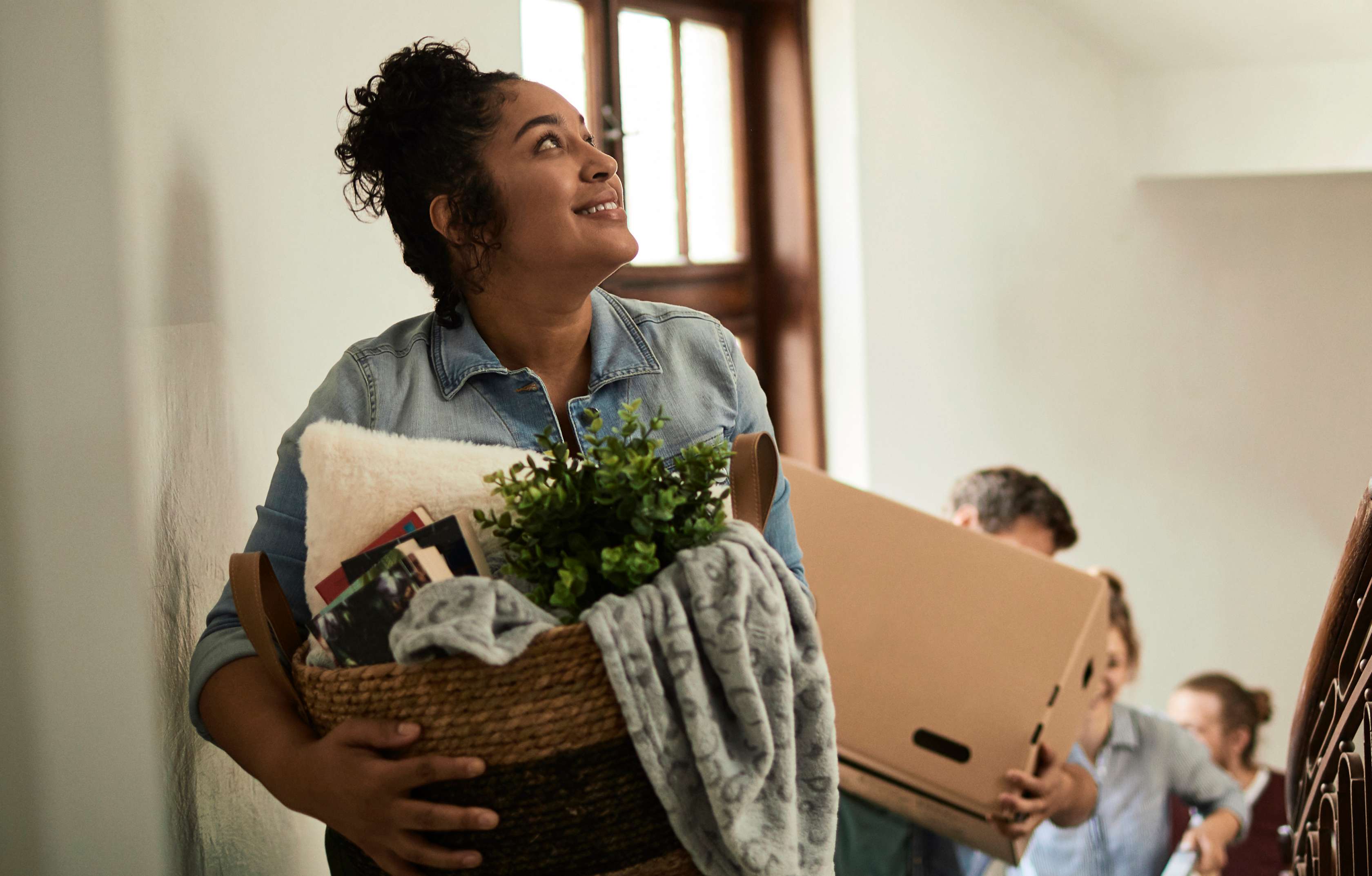 Gefälligkeitsschäden: Frau bringt einen Korb mit Dekoartikeln und Büchern die Treppe hoch im Hintergrund Umzugshelfer