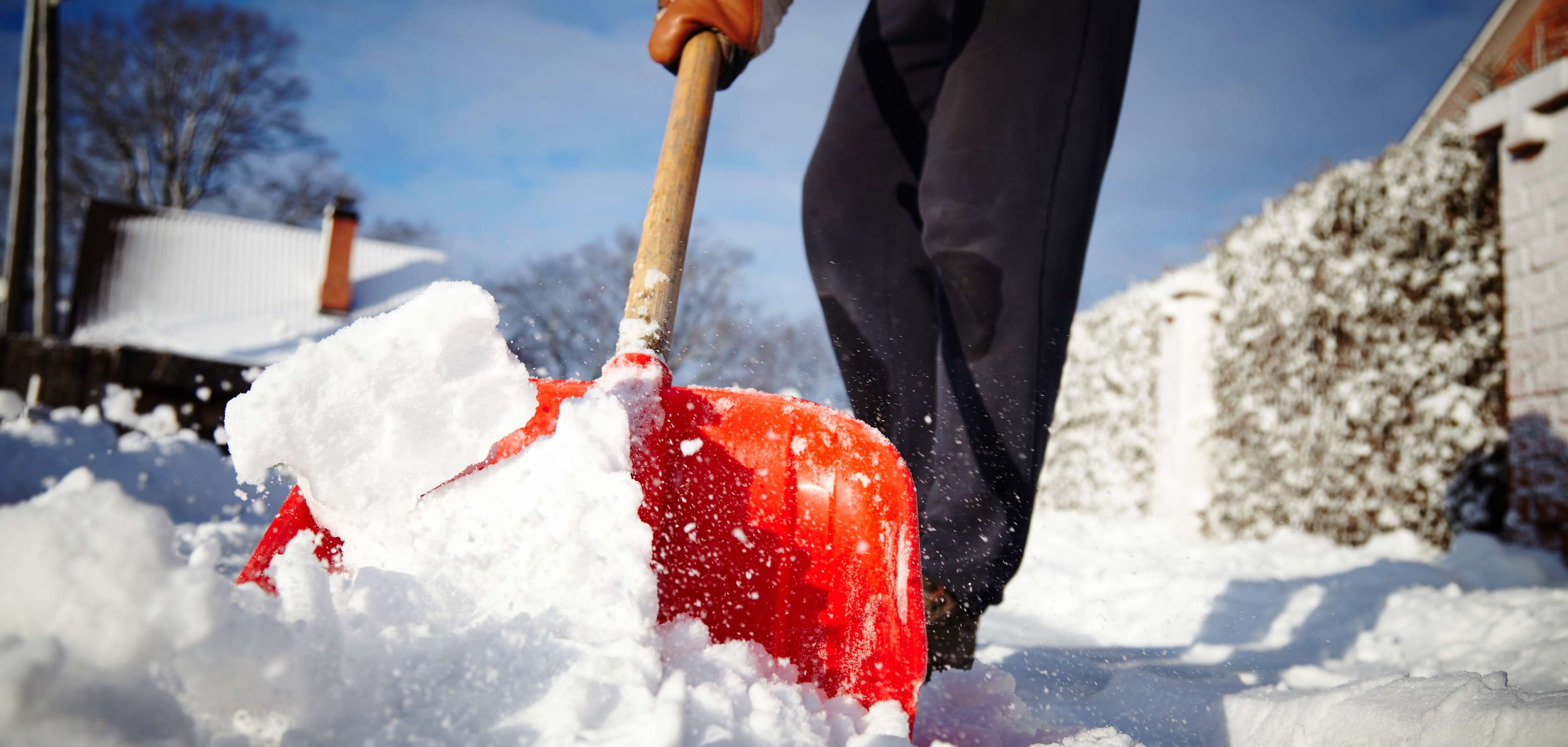 Schneeräumpflicht: Mann in schwarzer Hose und roter Schneeschaufel beim Schneeräumen 