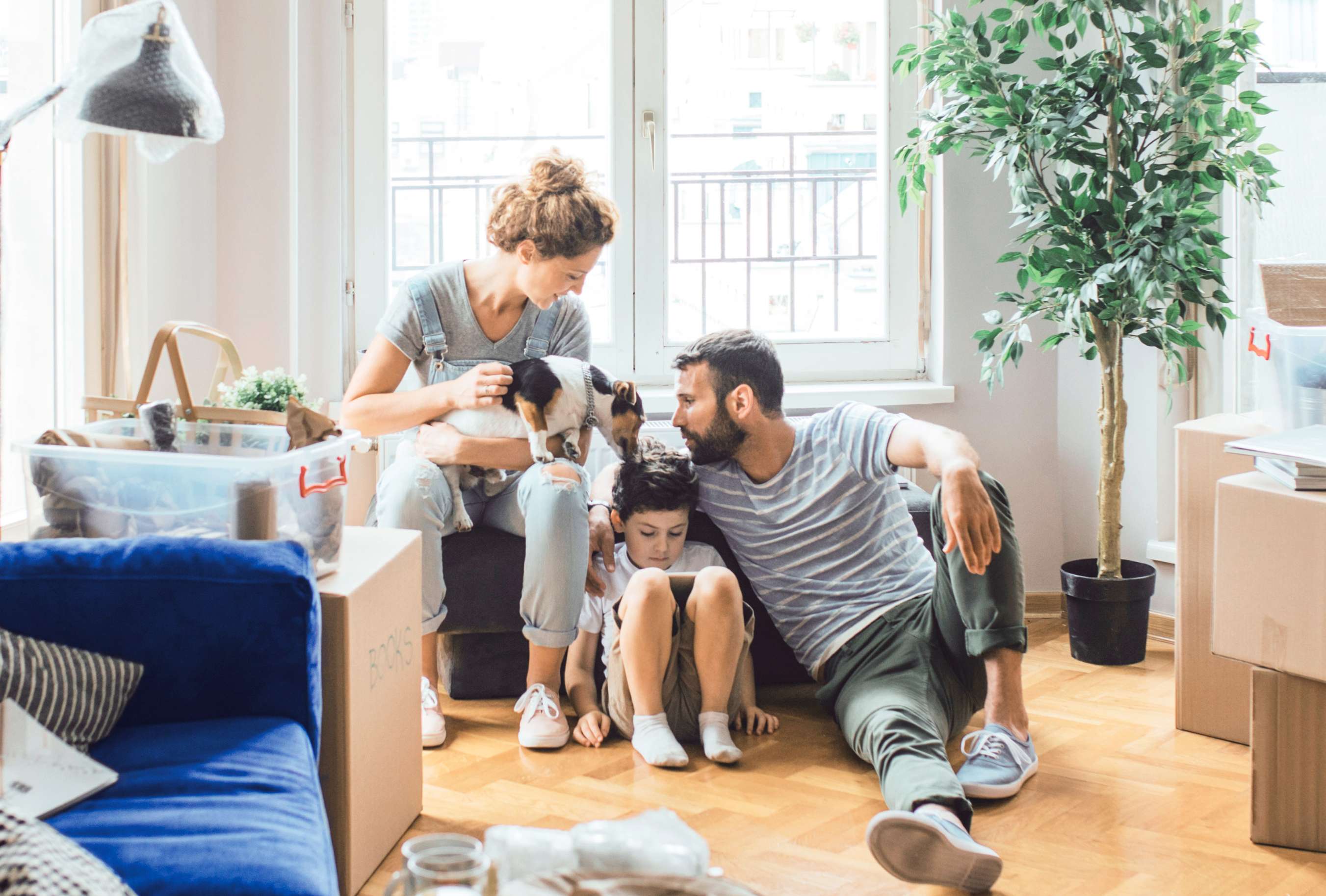 Privatschutz: Eine junge Familie sitzt zwischen Umzugskartons glücklich auf dem Fußboden