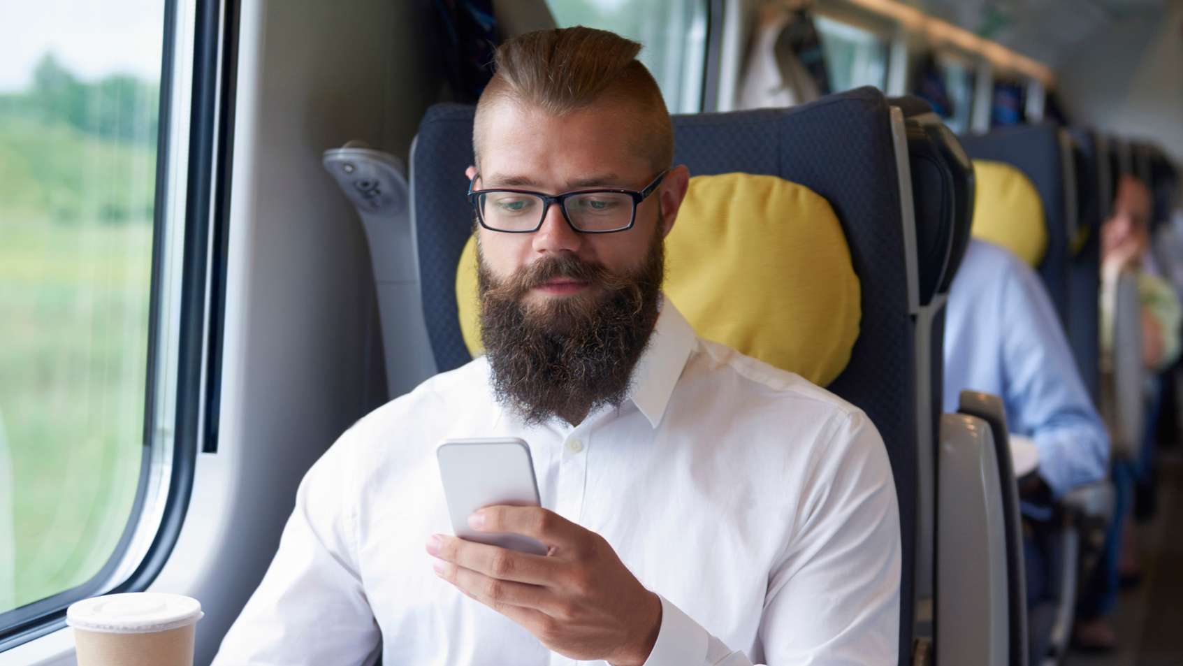 Mann mit Handy in der Hand sitzt in einem Zugabteil am Fenster