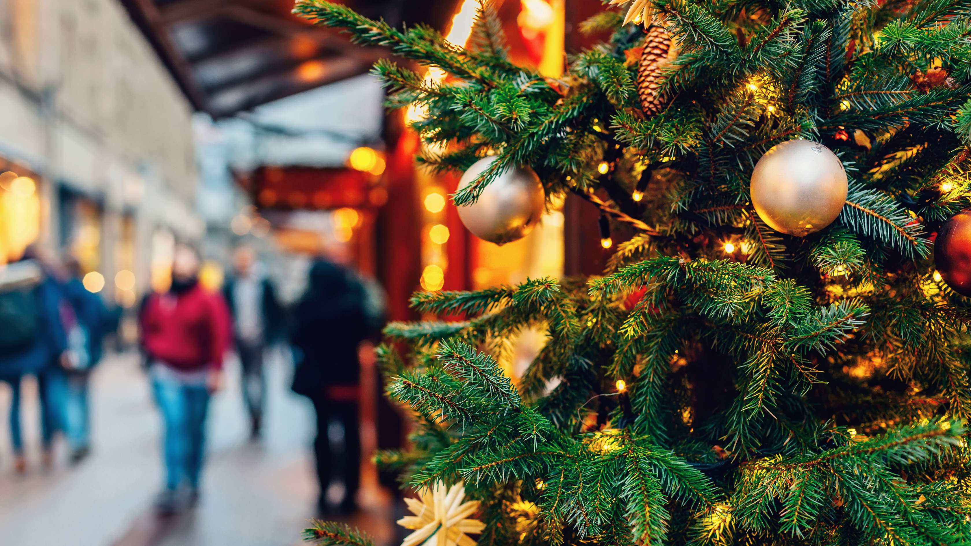 Szene auf einem Weihnachtsmarkt mit geschmücktem Christbaum im Vordergrund