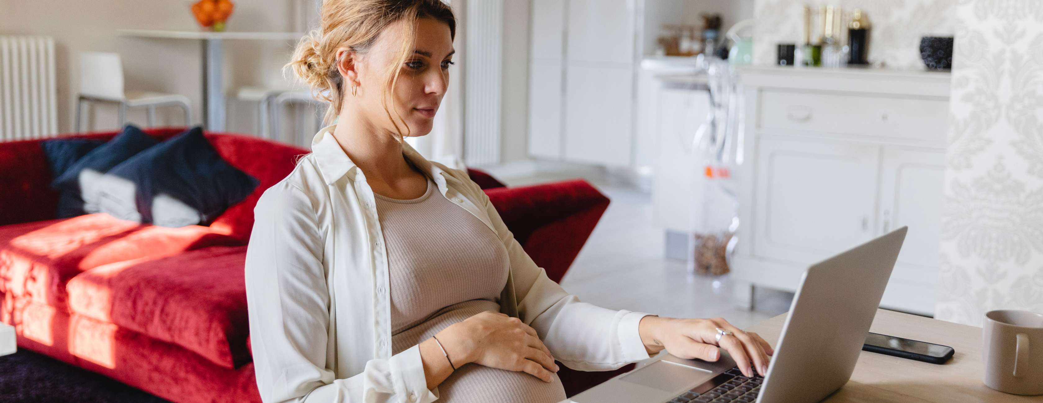 Schwangere Frau sitz am Schreibtisch mit einem Laptop