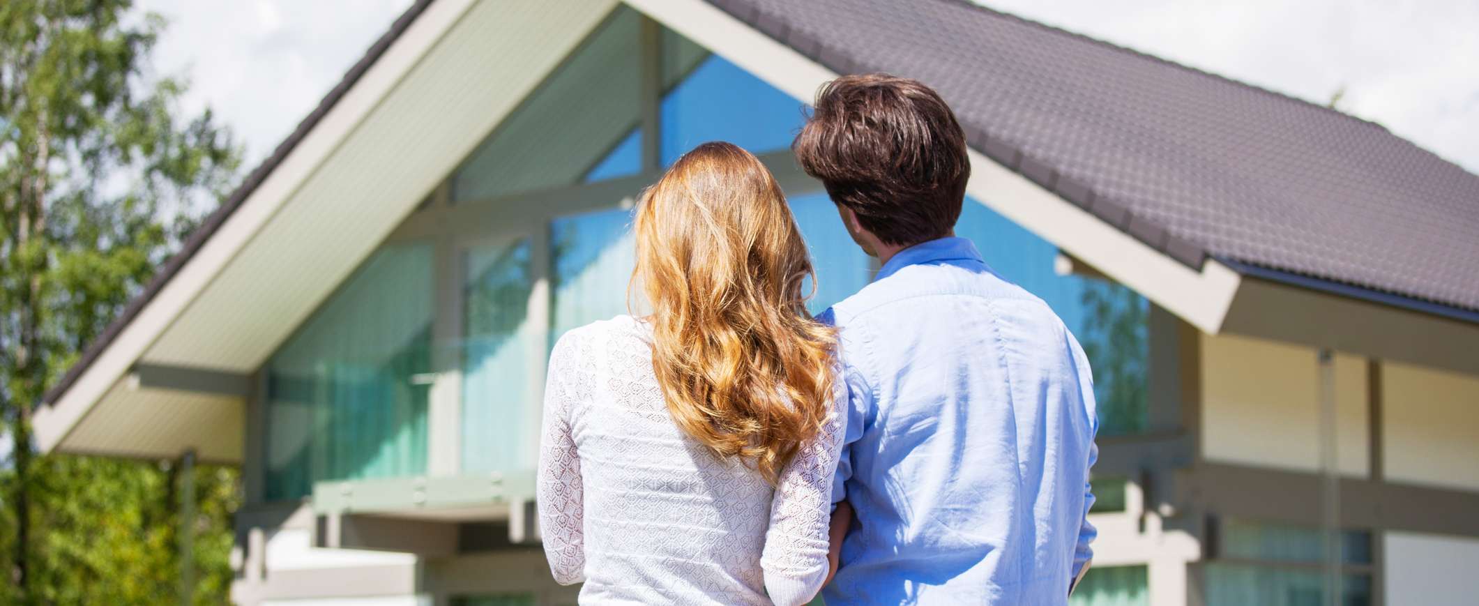 Ein Paar steht mit dem Rücken zur Kamera und schaut zu einem modernen Einfamilienhaus