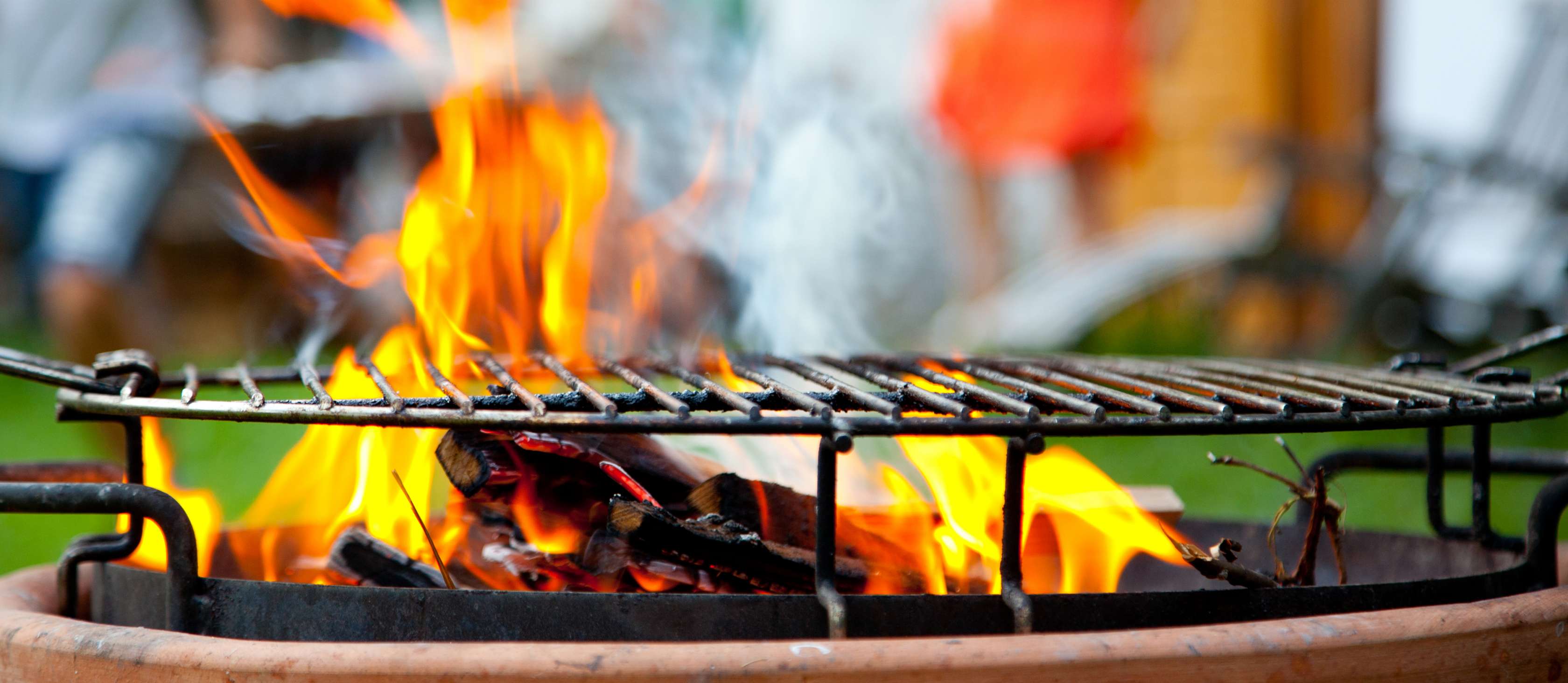 Offener, brennender und rauchender Grill mit Grillrost in einem Garten – Symbolbild für Grillen im Mehrfamilienhaus