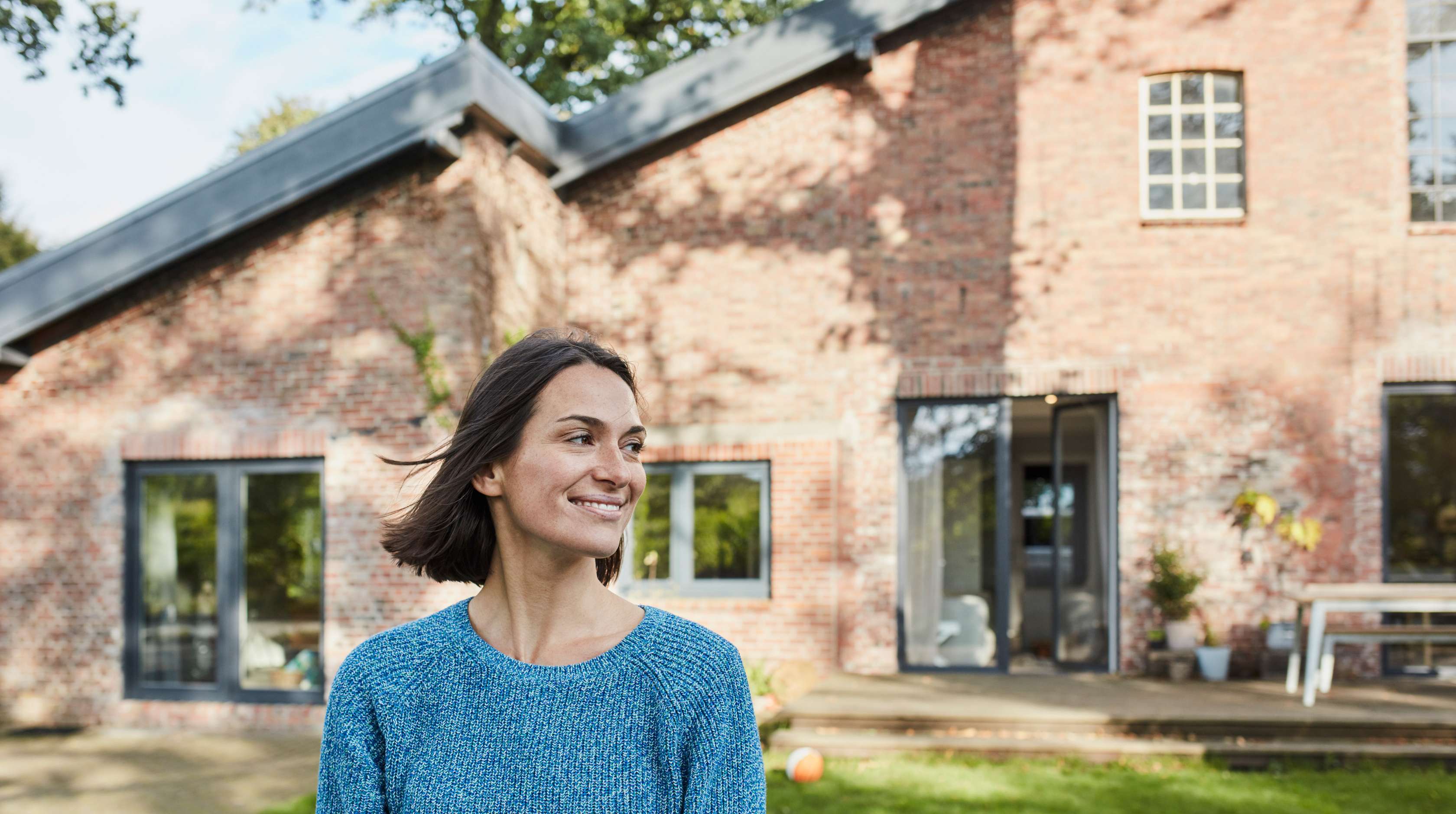Eine Frau steht lächelnd vor einem Einfamilienhaus