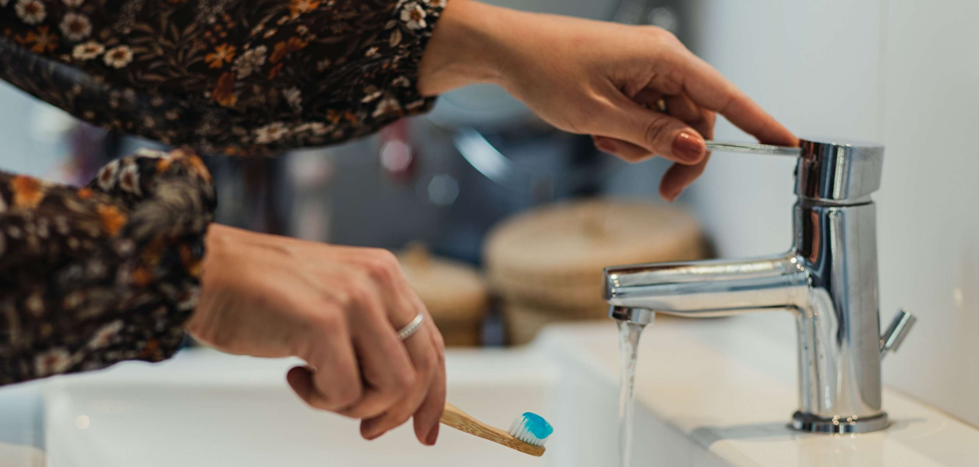 Frau hält Zahnbürste unter einen Wasserhahn