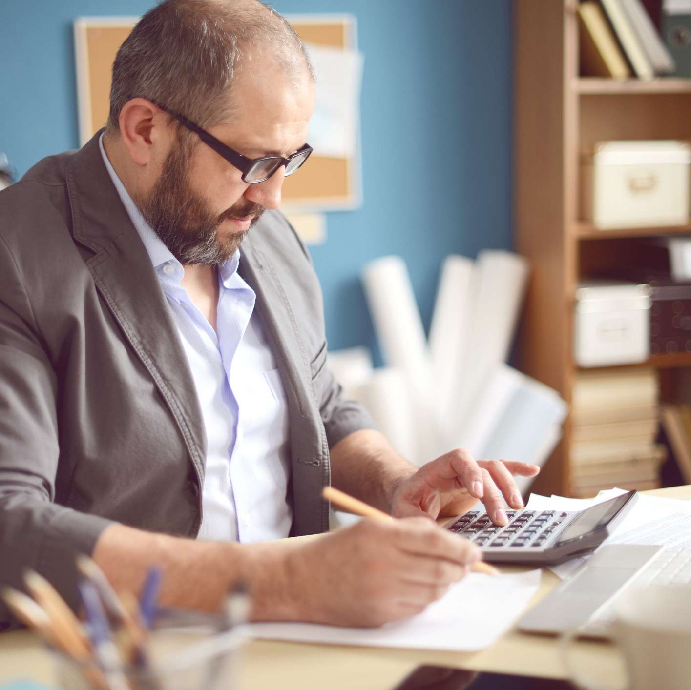 Allianz - Rechtsschutzversicherung steuerliche Absetzbarkeit: Mann sitzt am Schreibtisch vor Laptop und kalkuliert mit dem Taschenrechner