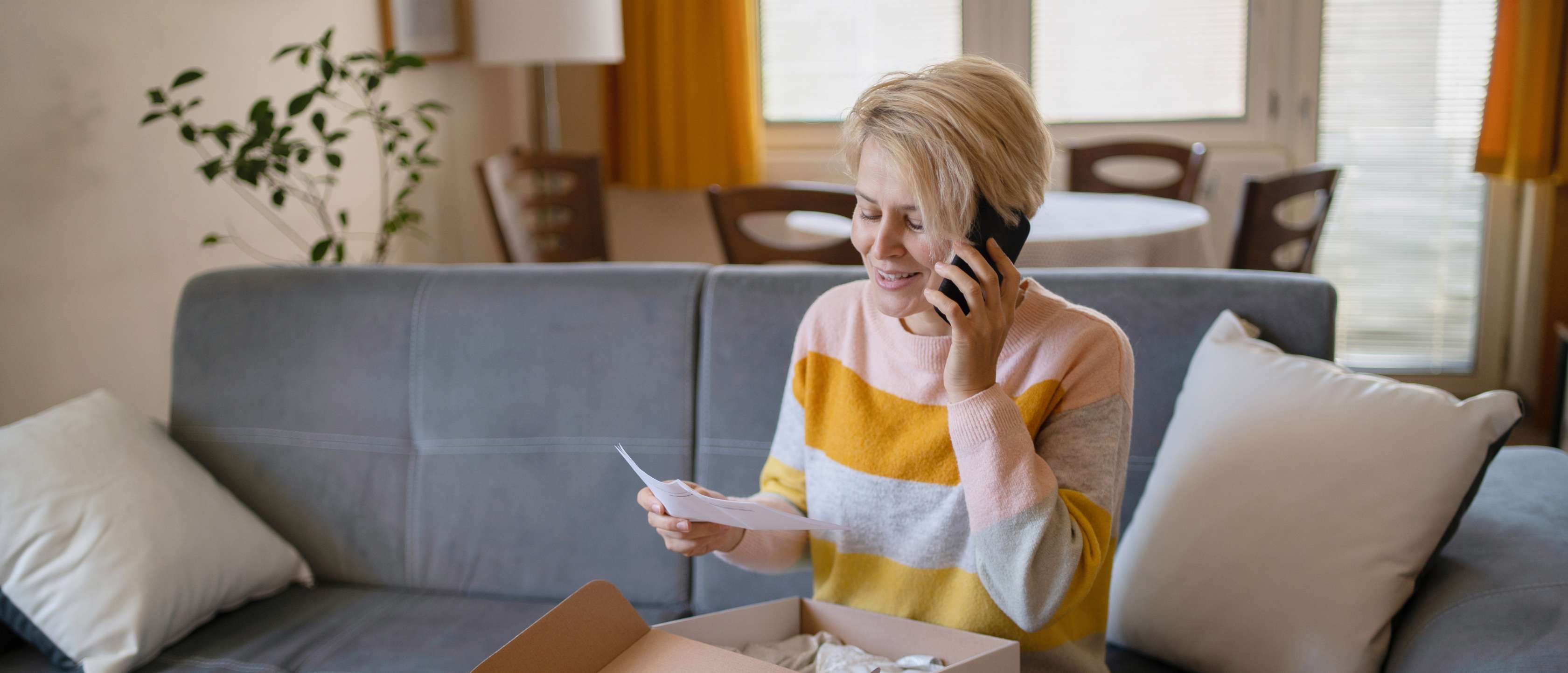 Garantie und Gewährleistung: Eine Frau sitzt mit einem Paket auf dem Sofa und telefoniert