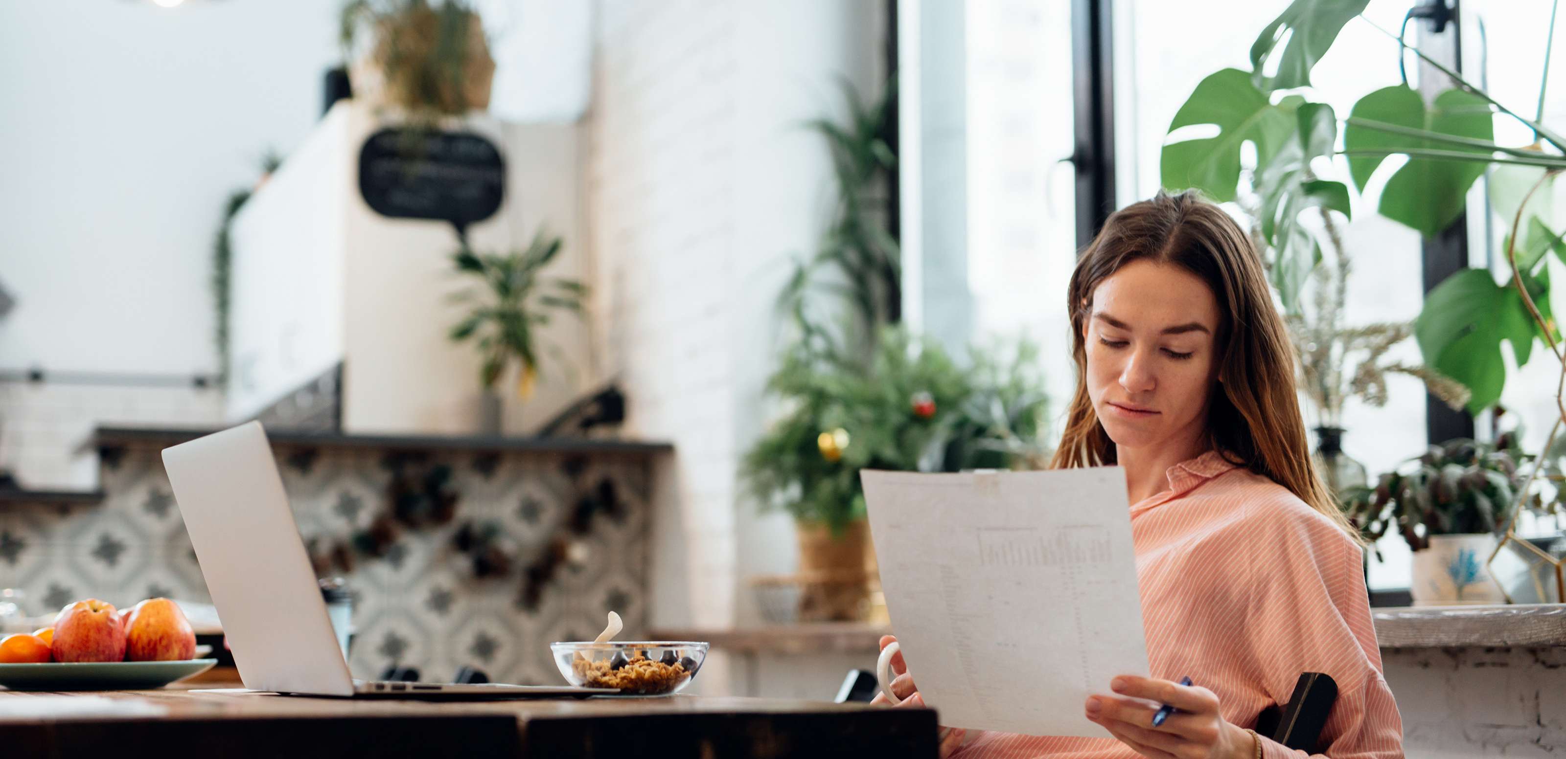 Eine junge Frau sitzt an ihrem Küchentisch und liest ein Dokument