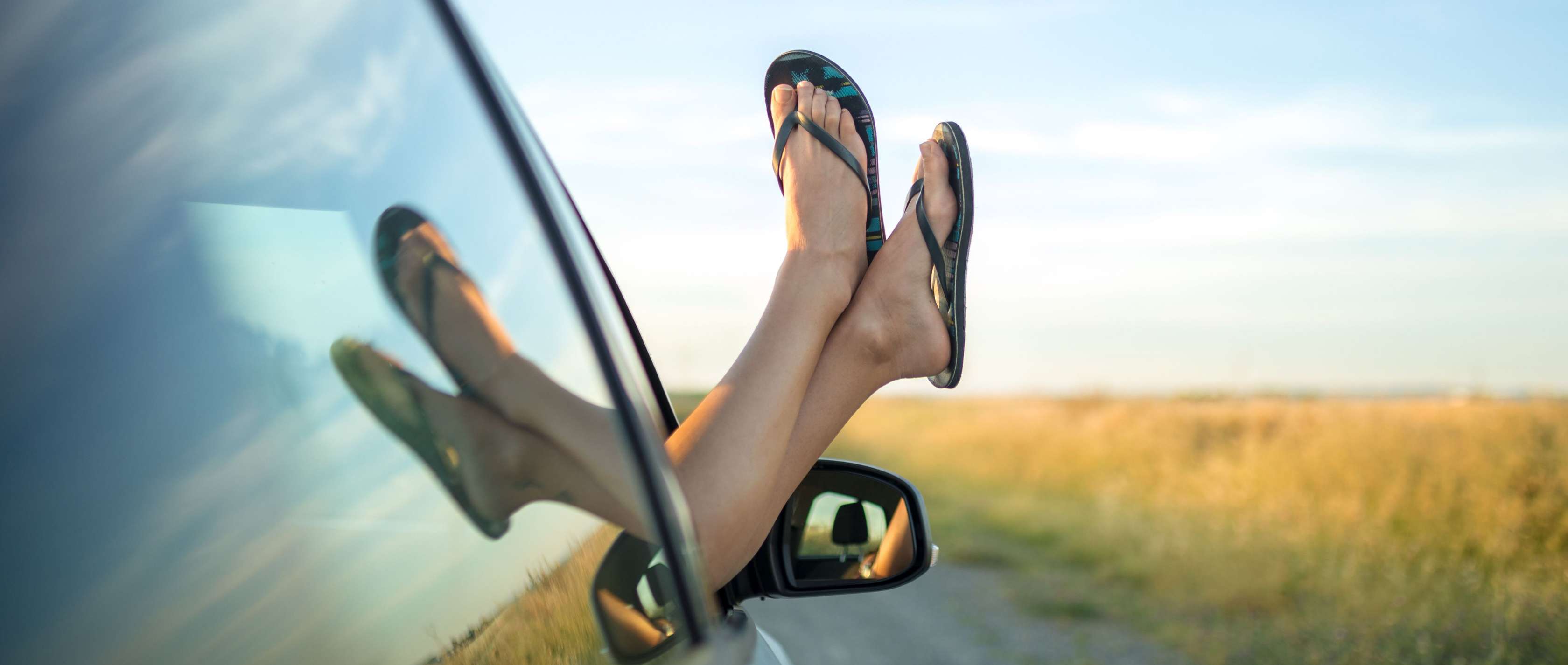Fahren mit Flip-Flops: Ein Paar Füße mit Flipflops werden aus einem Autofenster herausgestreckt
