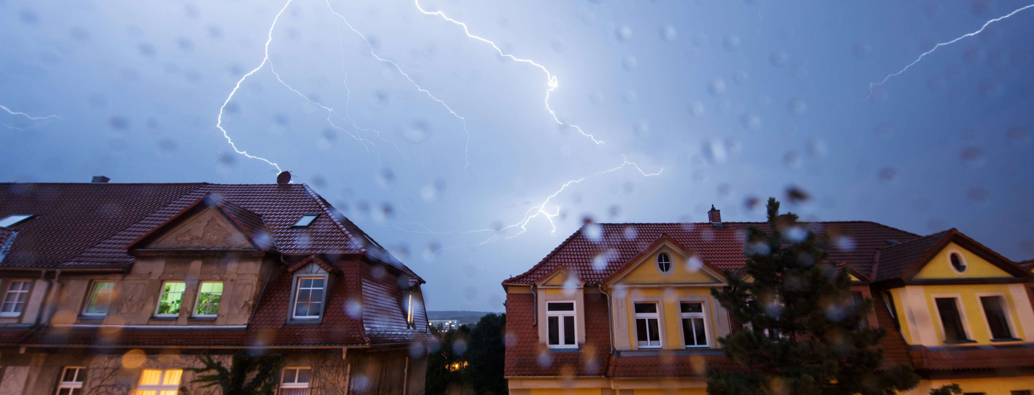 Vor Blitzeinschlag schützen: Blitze sind am Himmel über zwei Häusern zu sehen