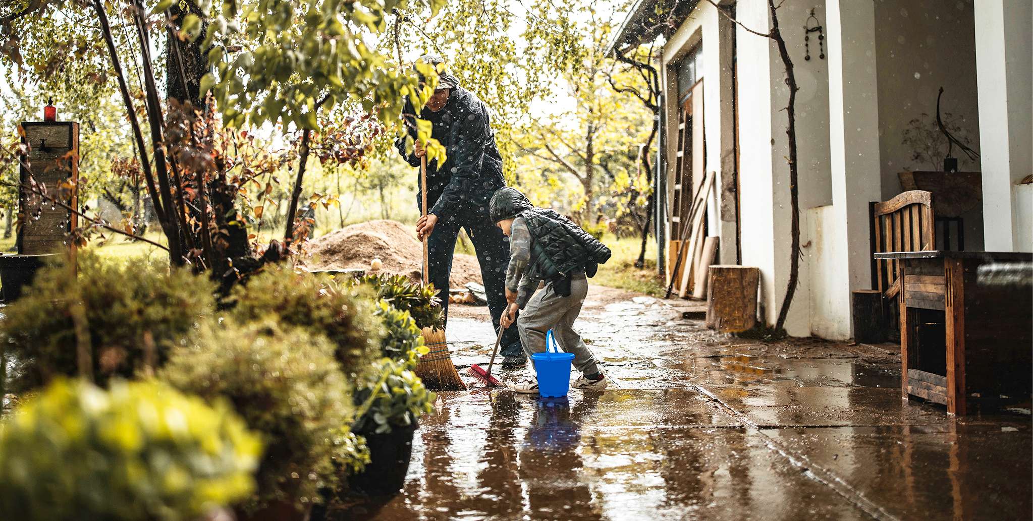 Elementarschutz: Vater und Sohn schaufeln im Regen Wasser vom Haus weg