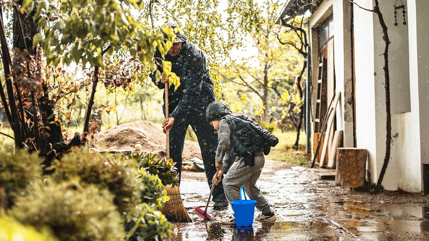 Elementarschutz: Vater und Sohn schaufeln im Regen Wasser vom Haus weg