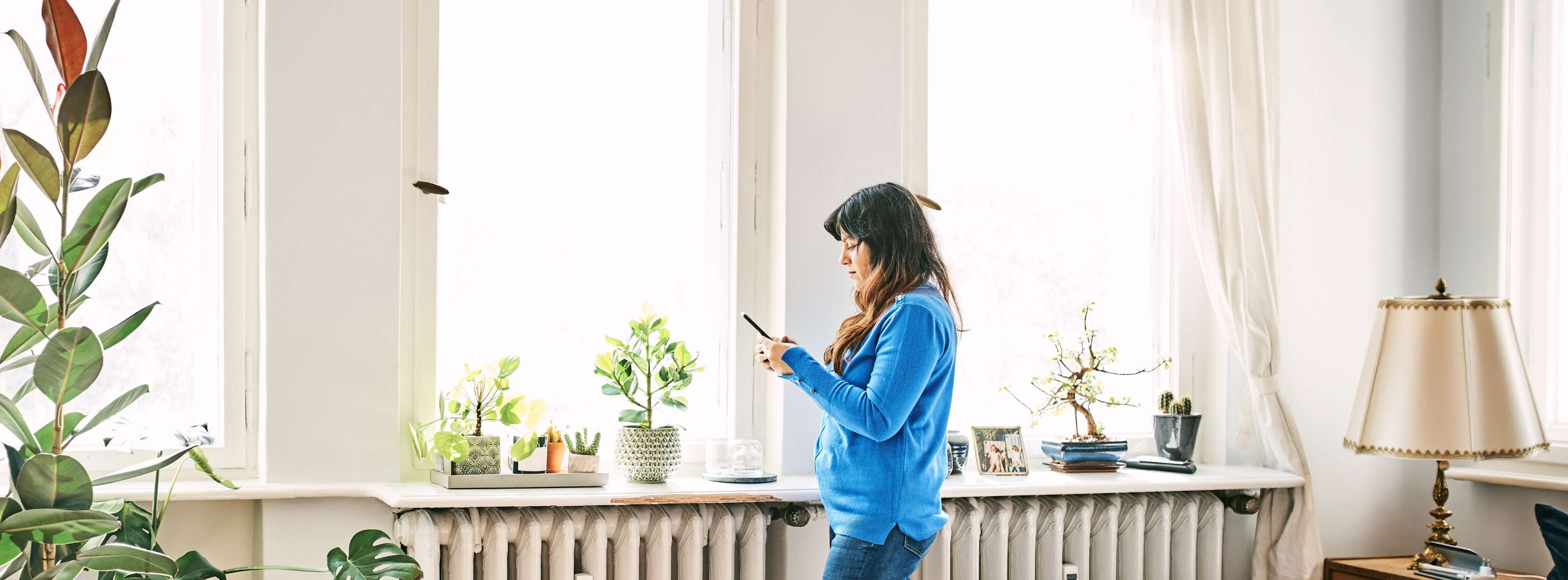 Öltankversicherung: Eine junge Frau steht an einer Heizung mit Handy