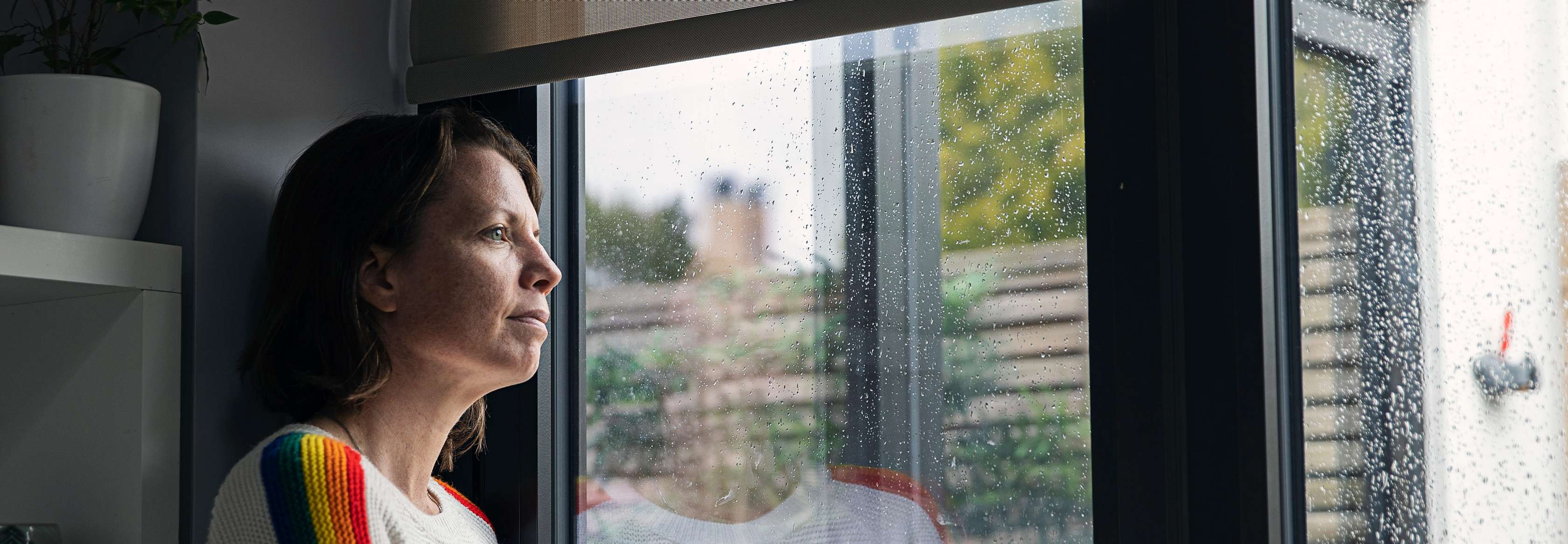 Eine Frau schaut sich ein Unwetter durch ein verregnetes Fenster an