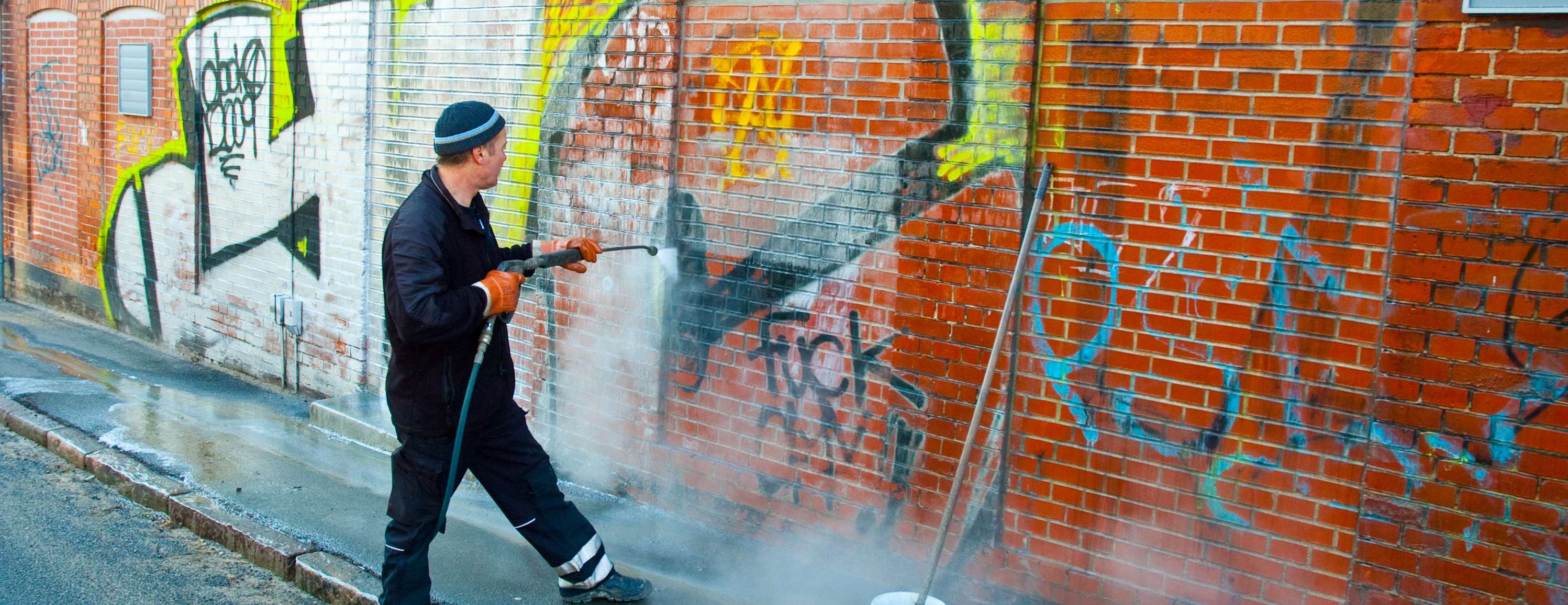 Mann in Arbeitsbekleidung entfernt Graffiti von roter Backsteinmauer