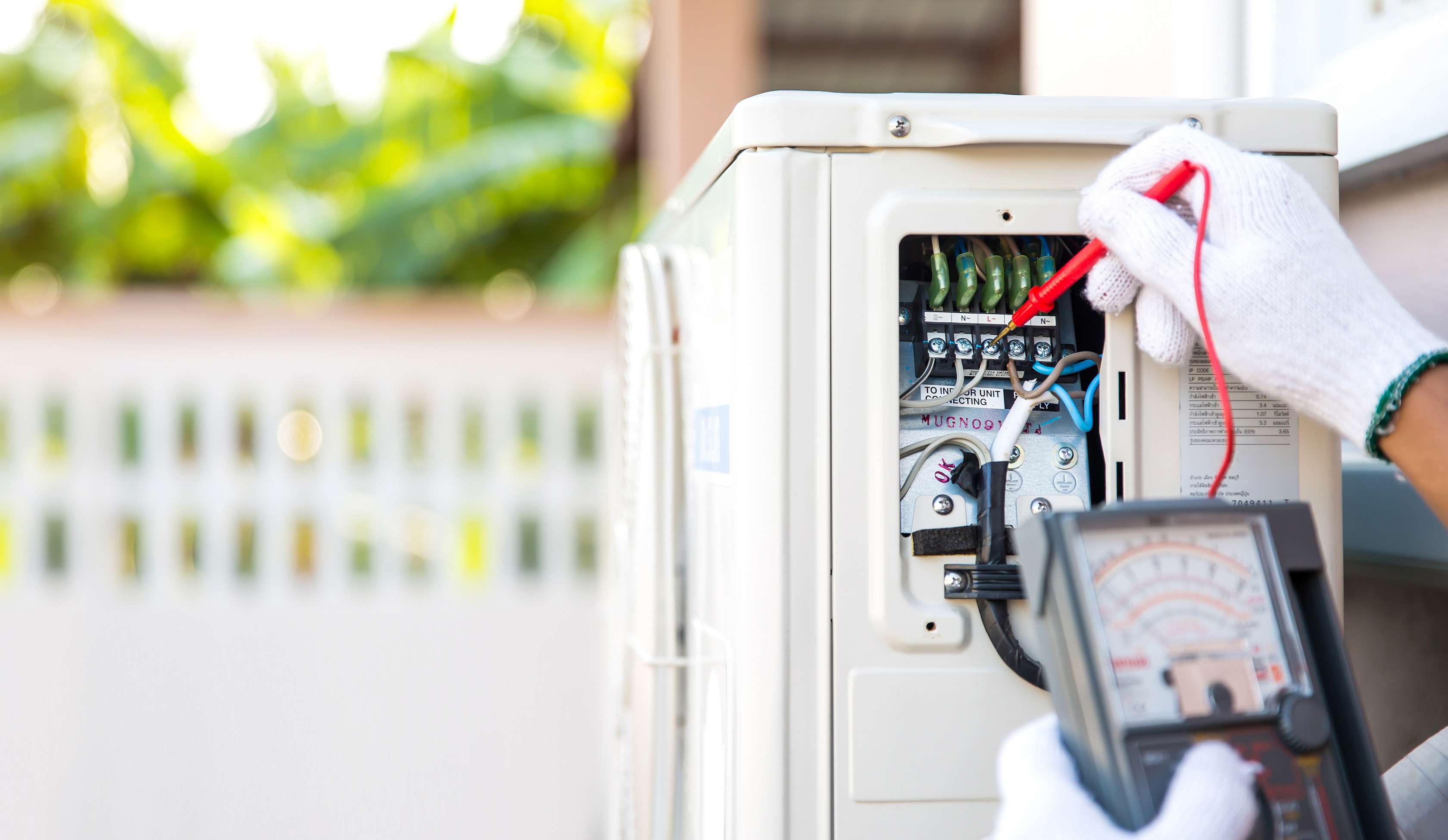 Wärmepumpe versichern: Installateur misst Spannung an Wärmepumpe im Garten