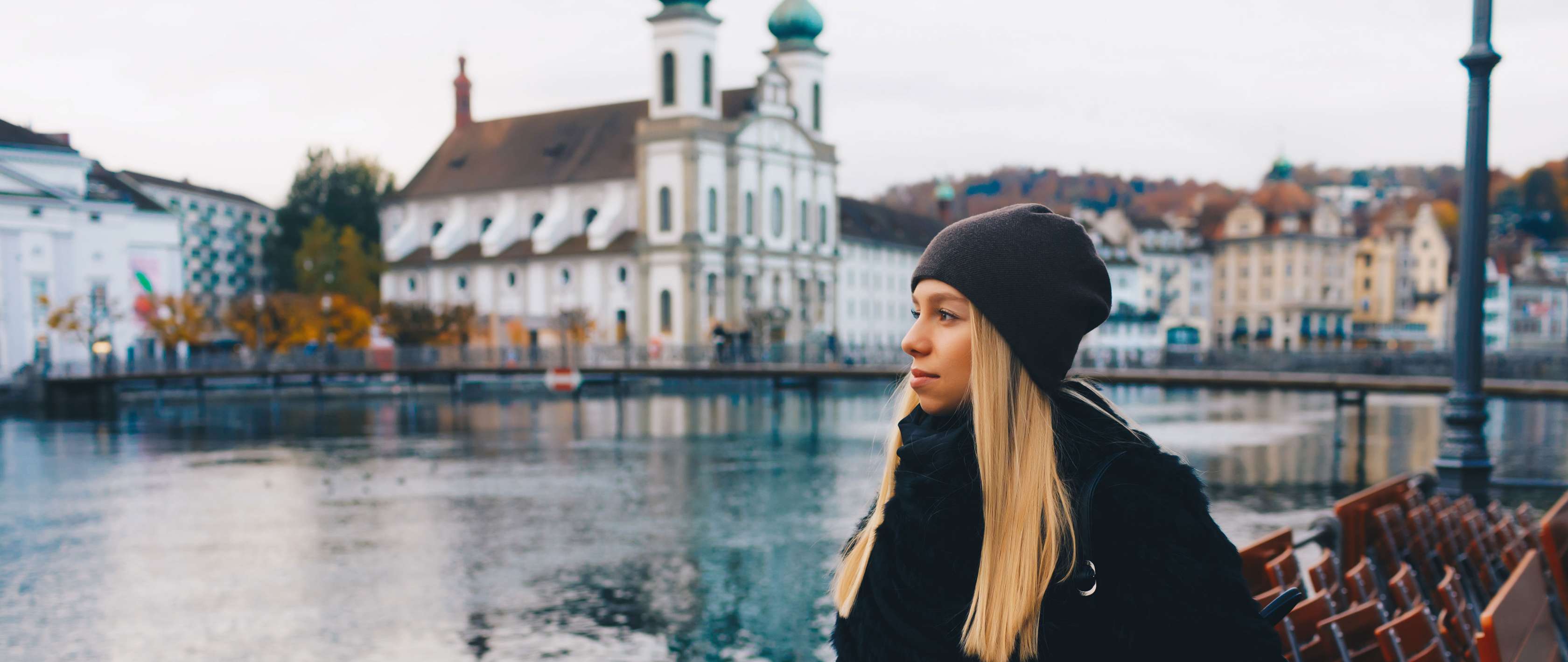 Frau in Luzern blickt auf den Fluss, hinter ihr ist eine Häuserreihe zu sehen