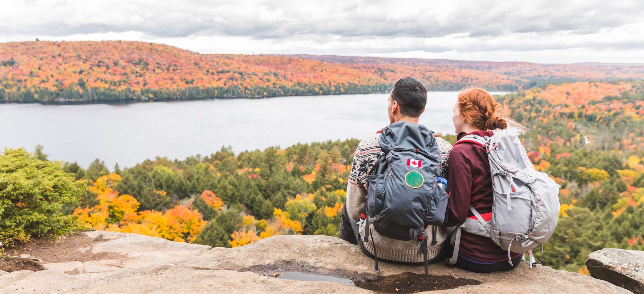 Junges Paar mit Rucksäcken sitzt auf einem Berg und sieht auf einen See