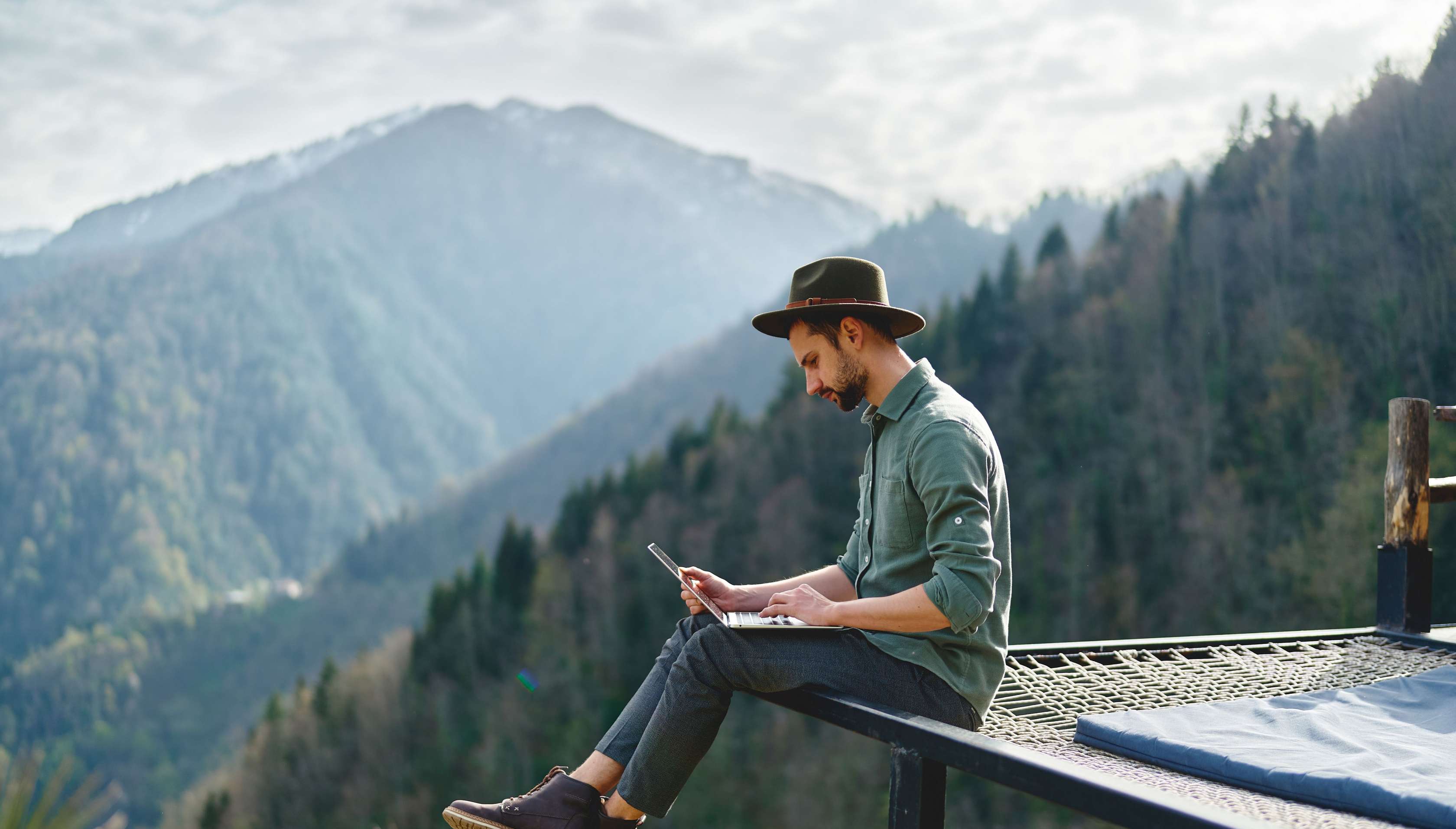 Meine Allianz | Ihre Versicherung online. Mann sitzt mit Laptop vor einer Bergkulisse