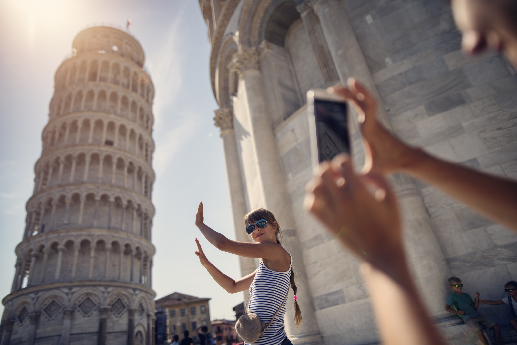Partner macht von Freundin ein Foto, wie sie ihre Hände in der Luft gegen den schiefen Turm von Pisa hölt. 