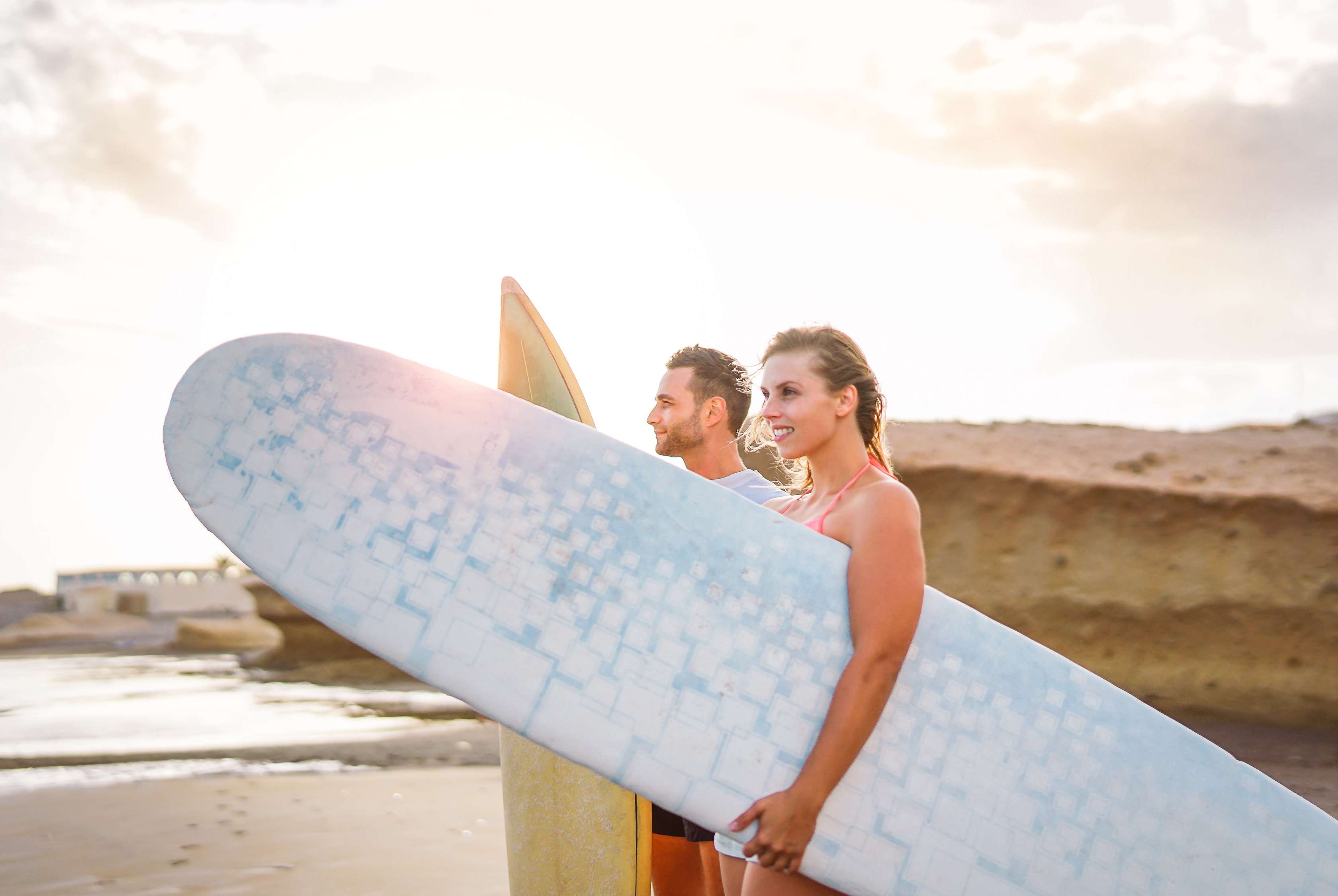 Ein Paar mit Surfbrettern unter dem Arm stehen am Strand und schauen auf das Meer
