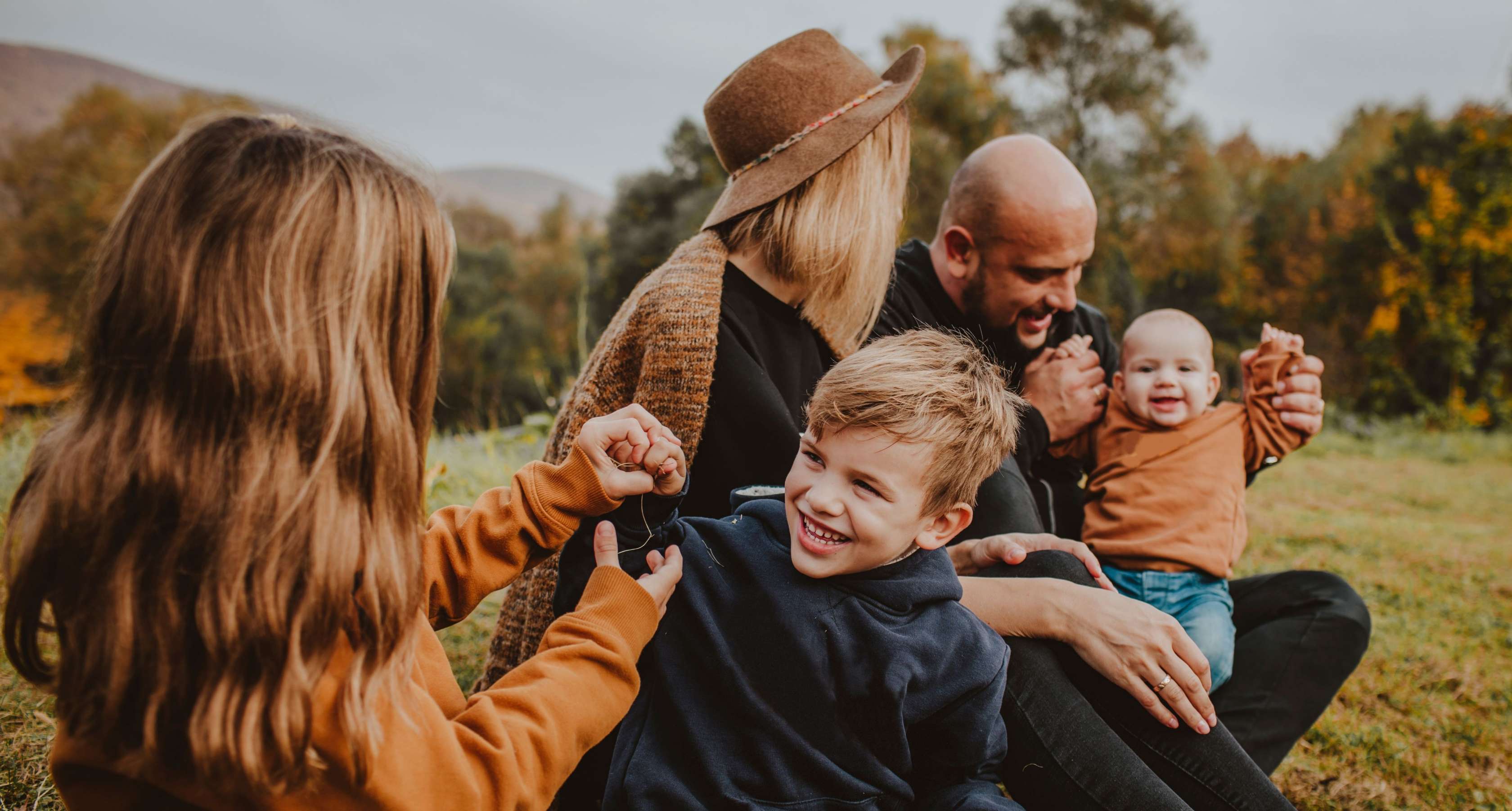Kinder & Familie: Eine Mutter und ein Vater sitzen gemeinsam mit ihren drei Kindern auf einer Wiese und haben Spaß.
