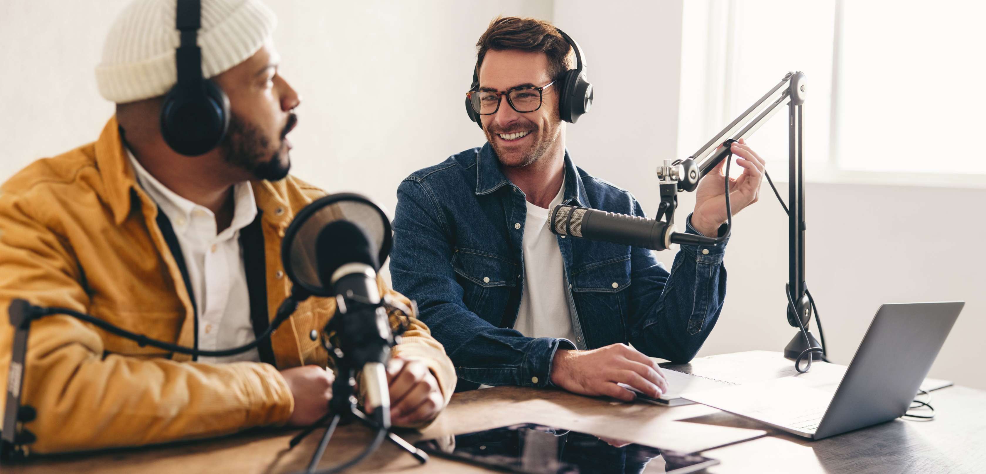 Livetalks und Podcasts: Zwei Männer mit Kopfhörer schauen sich lächelnd an während sie einen Podcast aufnehmen