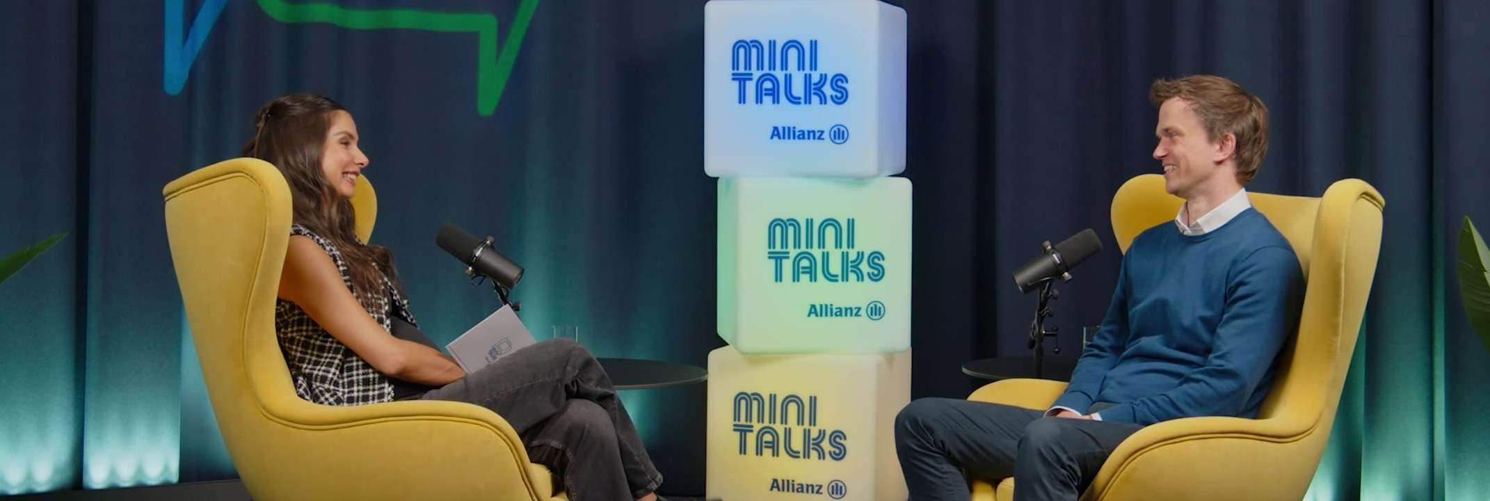 Allianz MiniTalks Folge 16 Schwankungen am Kapitalmarkt: Lea Wagner und Arne sitzen im Studio auf zwei Sesseln.