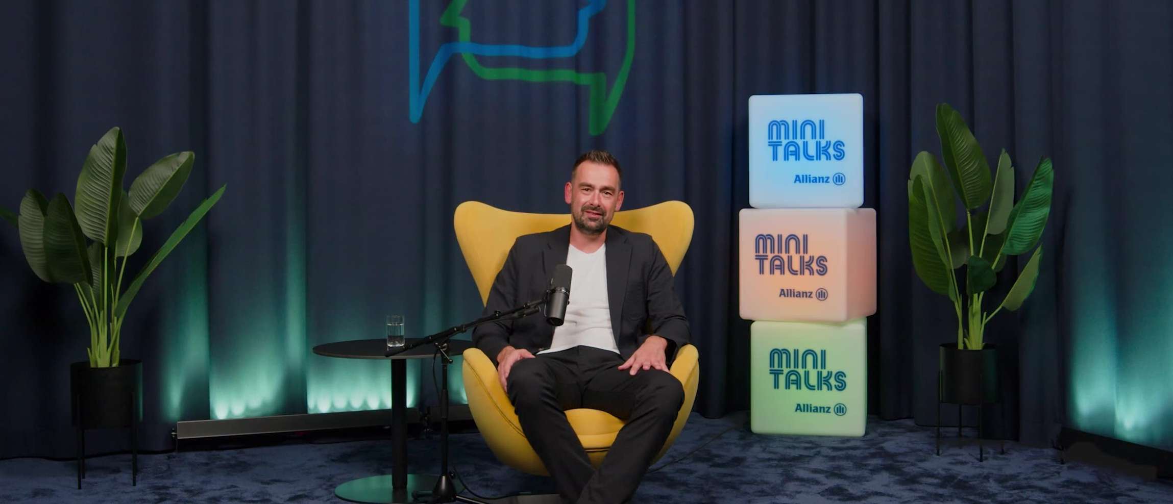 Allianz MiniTalks Folge 19 Altersvorsorgedepot: Wer bekommt die 540 Euro vom Staat?: Stefan sitzt im Studio auf einem Sessel.