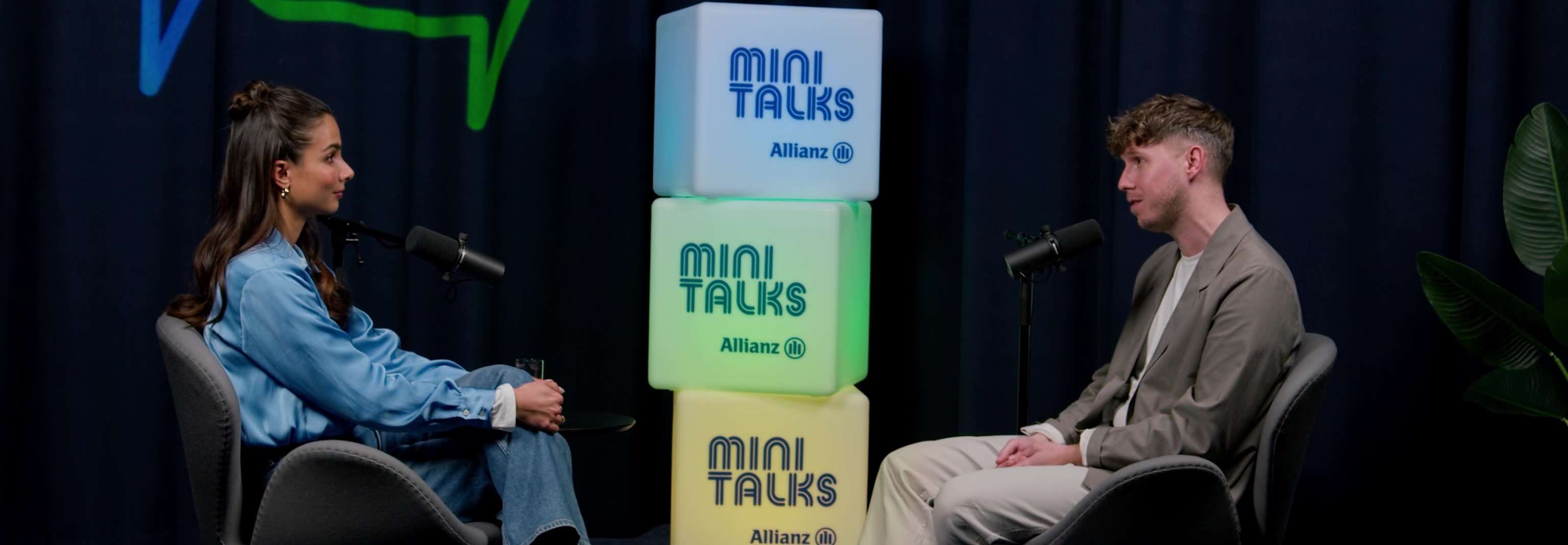 Allianz MiniTalks Folge 3 Grundlagen des Investierens: Lea Wagner und Sascha sitzen im Studio auf zwei Sesseln.