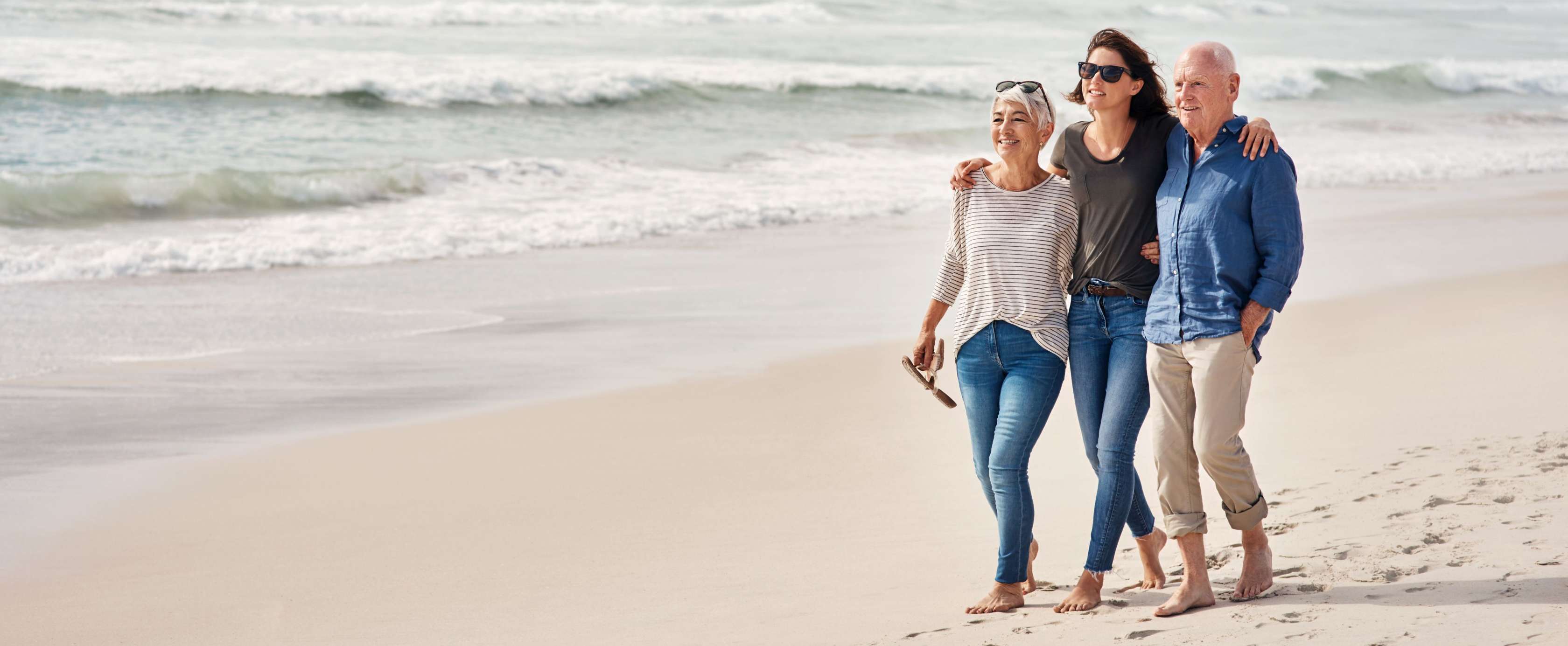 Allianz - Vorsorge- und Nachlassplanung: Ehepaar geht mit erwachsener Tochter am Strand spazieren