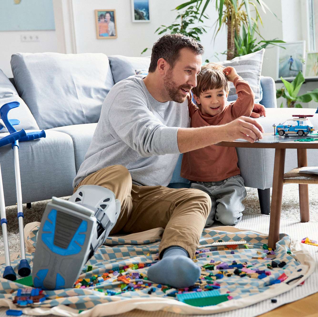 Allianz - Mann auf Krücken spielt mit Sohn im Wohnzimmer