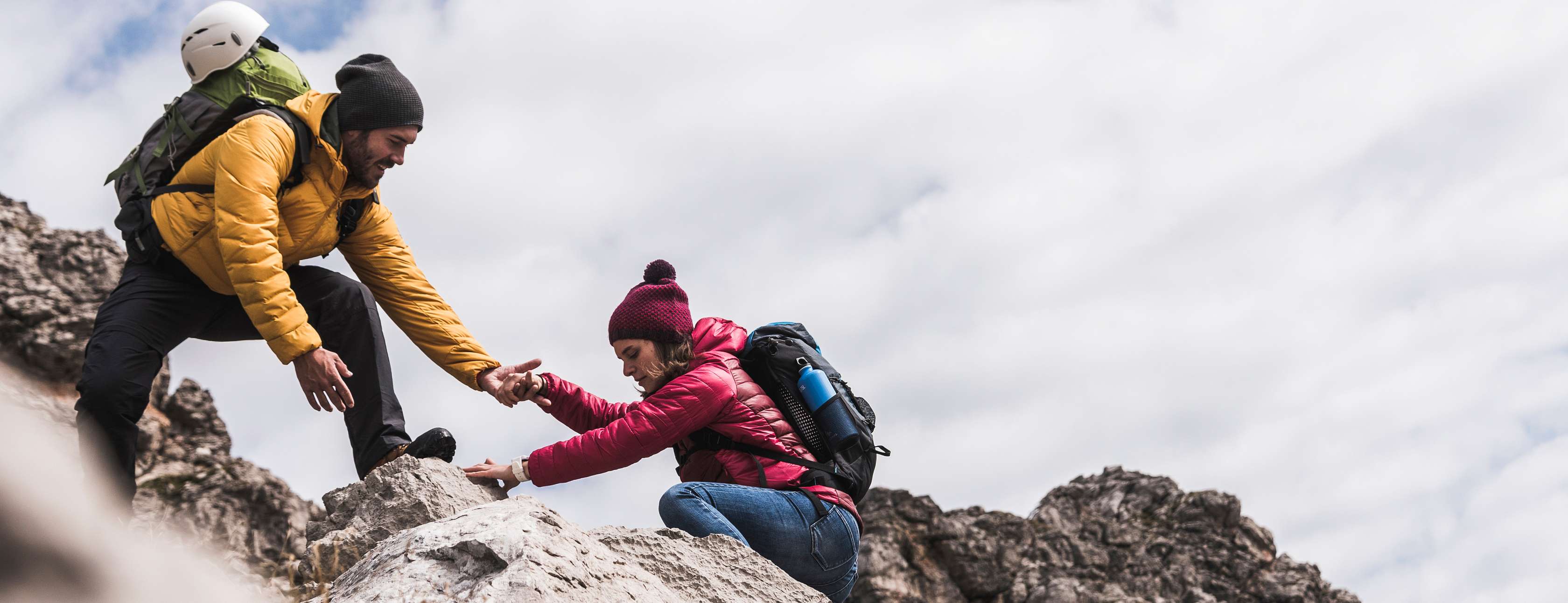 Allianz InvestFlex mit StrategieDepots: Ein Mann hilft einer Frau dabei, felsiges Terrain hinaufzuklettern.