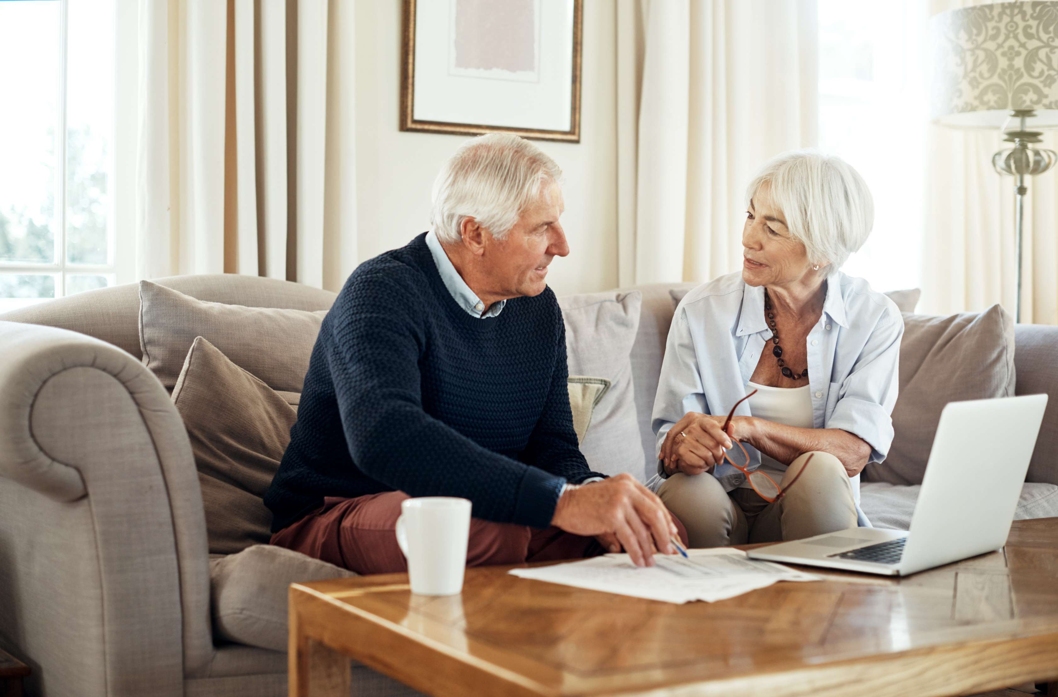 Älteres Paar sitzt auf Couch und schaut auf Unterlagen