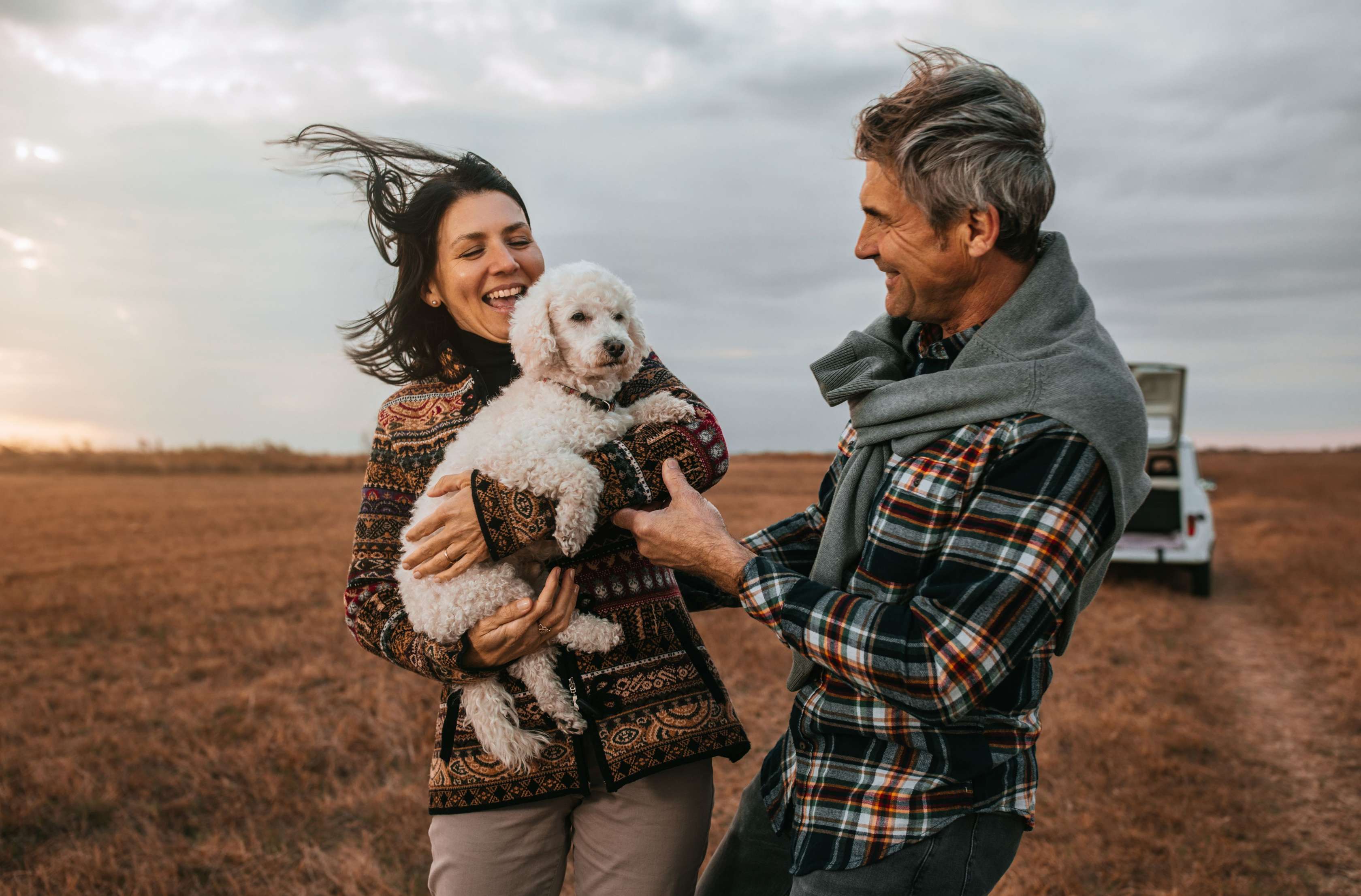 Mit der Allianz den Ruhestand planen: Ein Paar mit einem Hund steht lachend auf einem Feld.