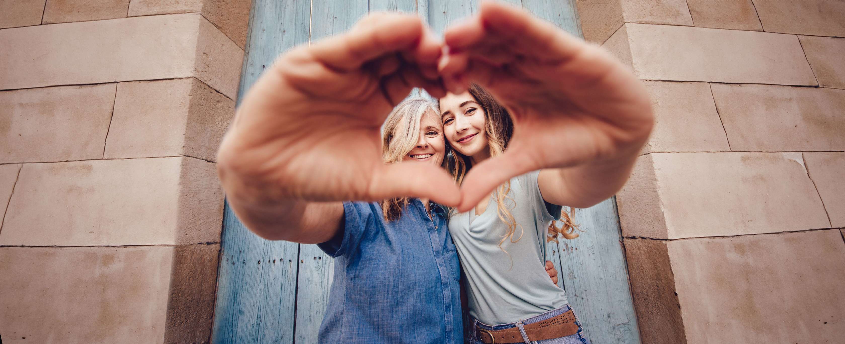 Allianz Sterbegeldversicherung – Mutter und Tochter lächeln in die Kamera und bilden mit ihren Händen zusammen ein Herz.