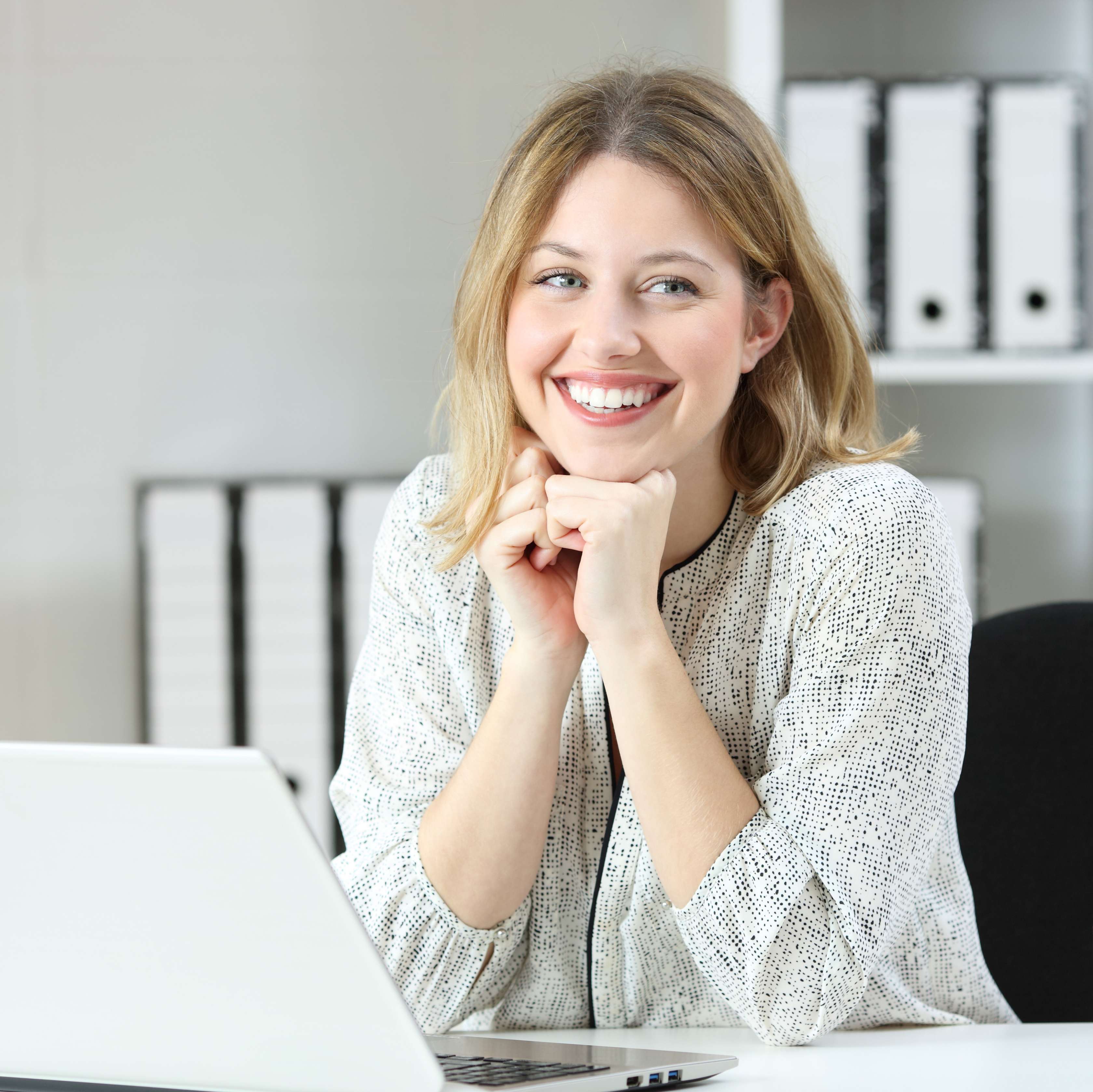 Junge Frau sitzt lächelnd mit einem Laptop am Schreibtisch