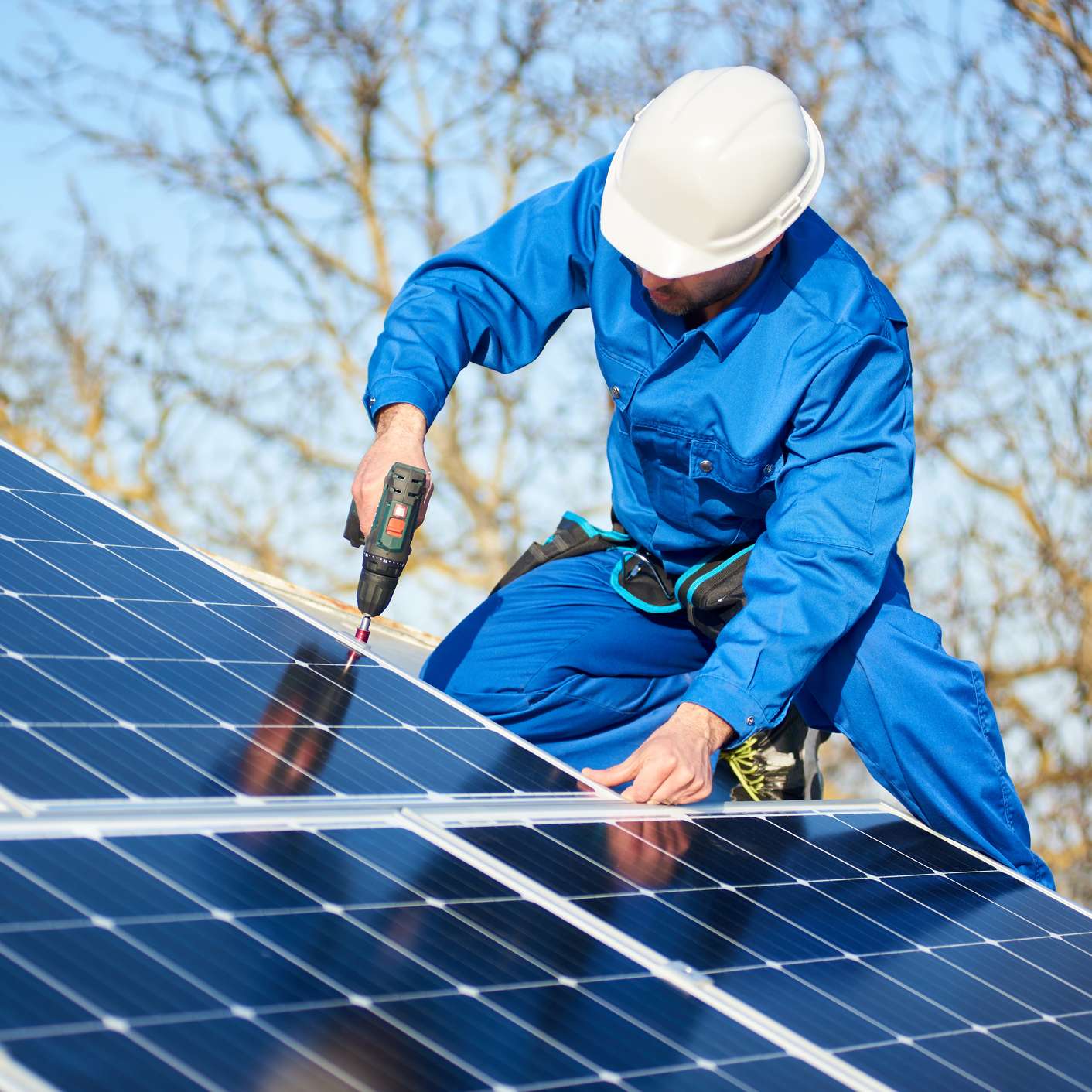 Ein Handwerker schraubt Solarpaneele auf ein Hausdach