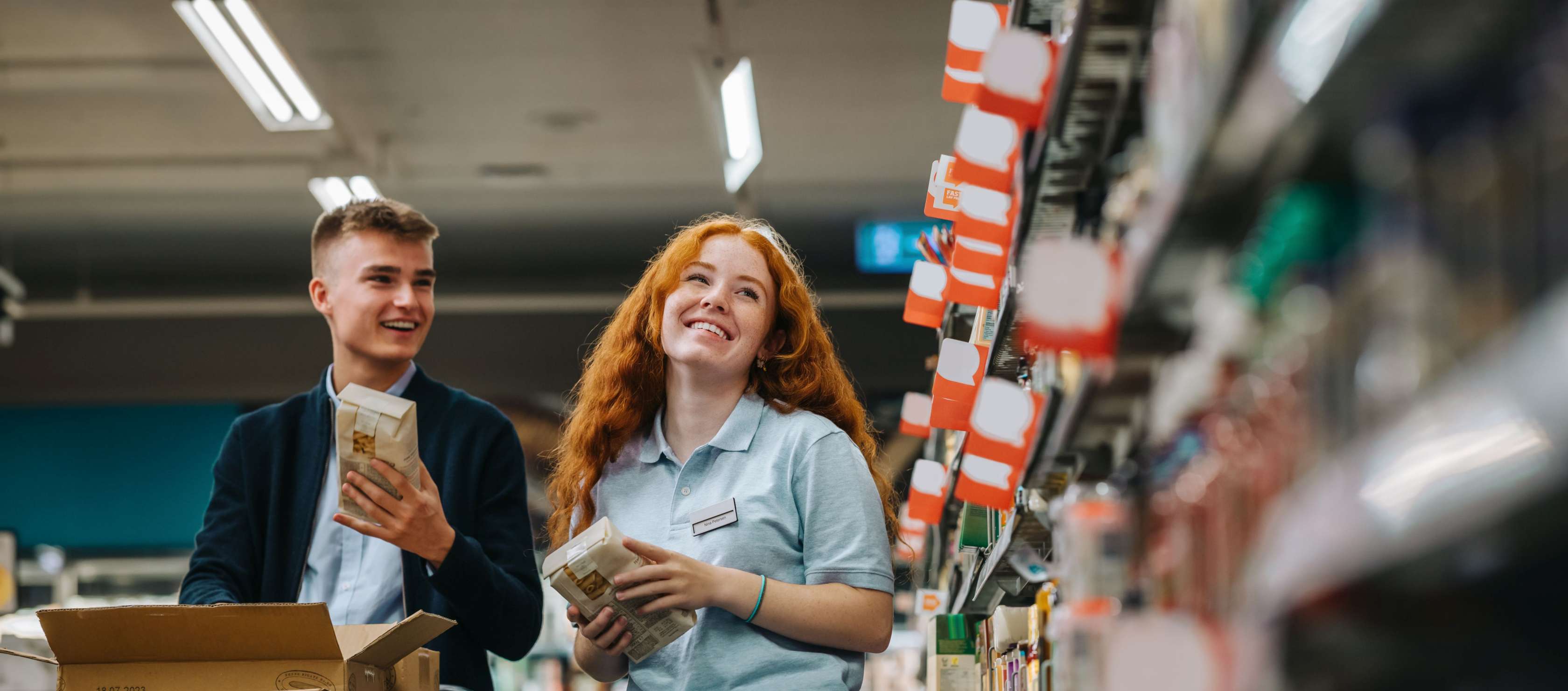 Ein junger Mann und eine junge Mitarbeiterin stehen zwischen Supermarktregalen.