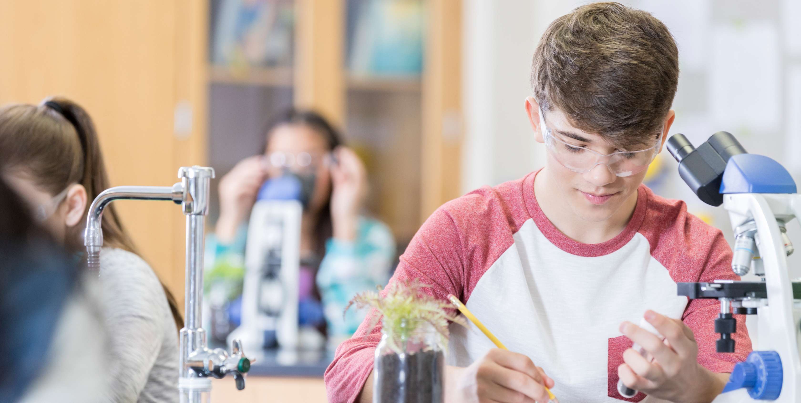 Berufsunfähigkeitsversicherung für Schüler - Schüler sitzt vor einem Mikroskop und notiert etwas