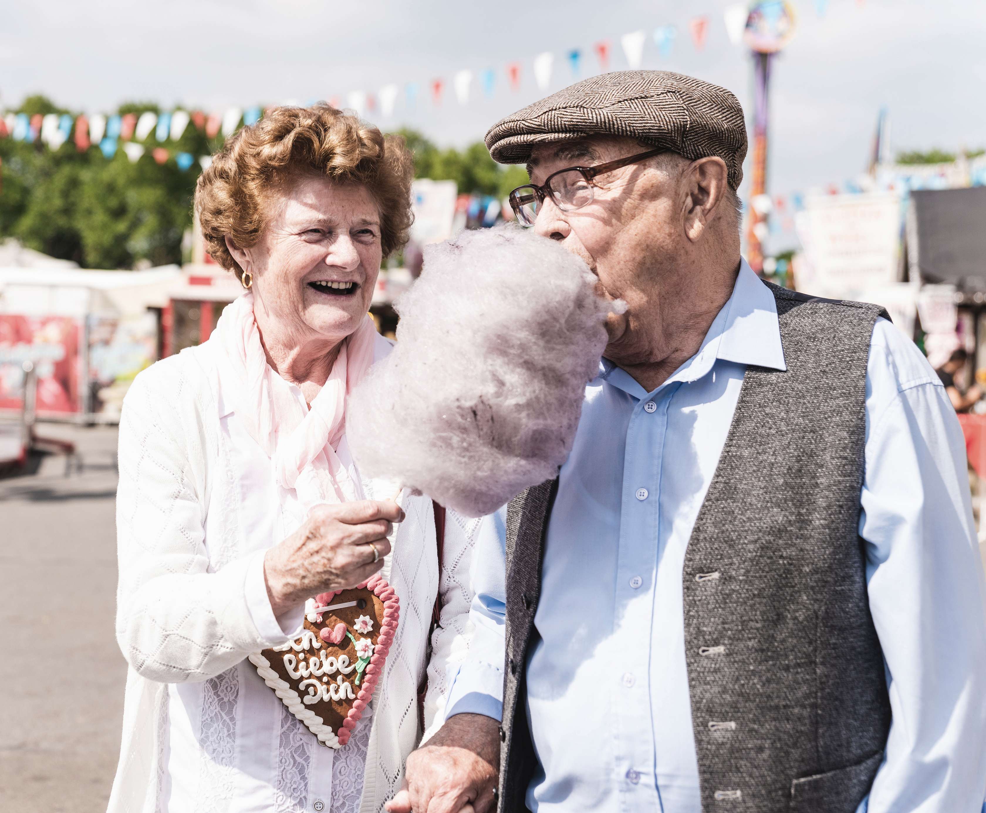 Berufsunfähigkeitsversicherung - Steuer: Glückliches altes Ehepaar auf dem Jahrmarkt mit Zuckerwatte und Lebkuchenherz