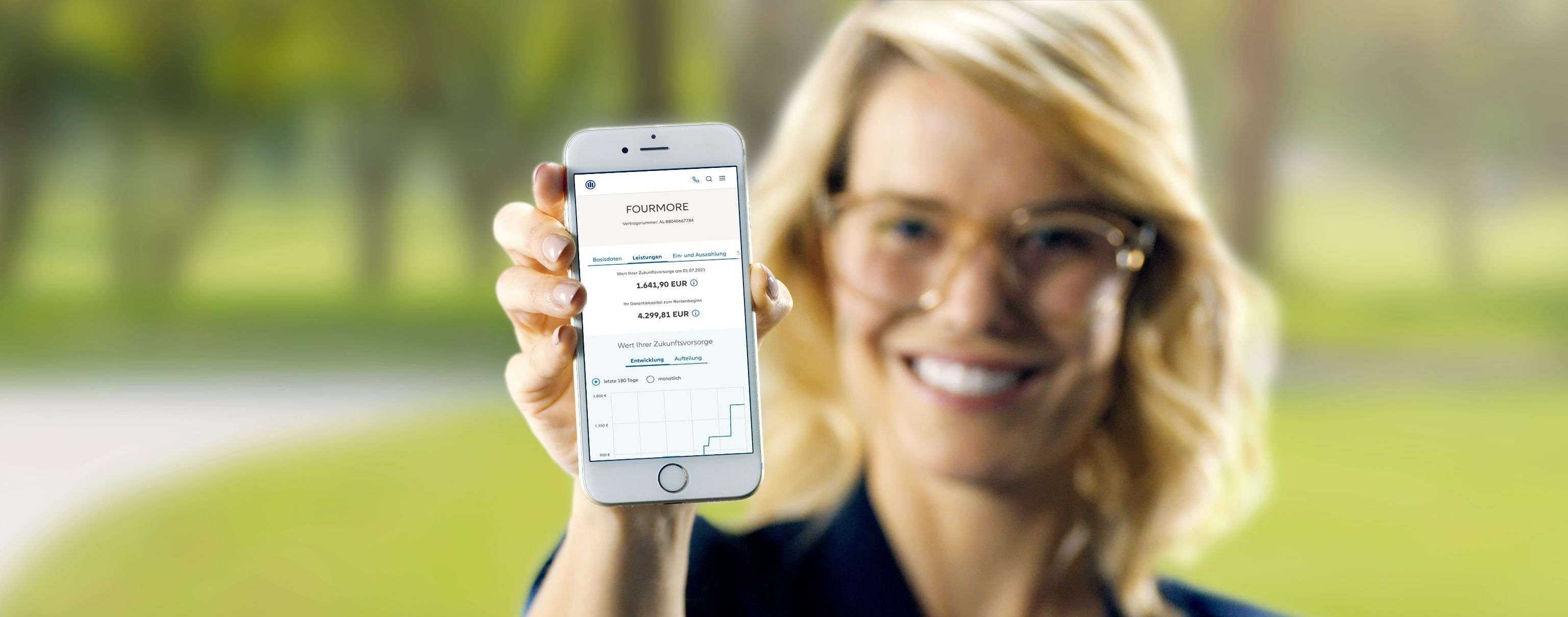 Allianz Fourmore - Eine lächelnde Frau mit Brille hält ein Smartphone in die Kamera, auf dem unscharfe Textnachrichten zu sehen sind.