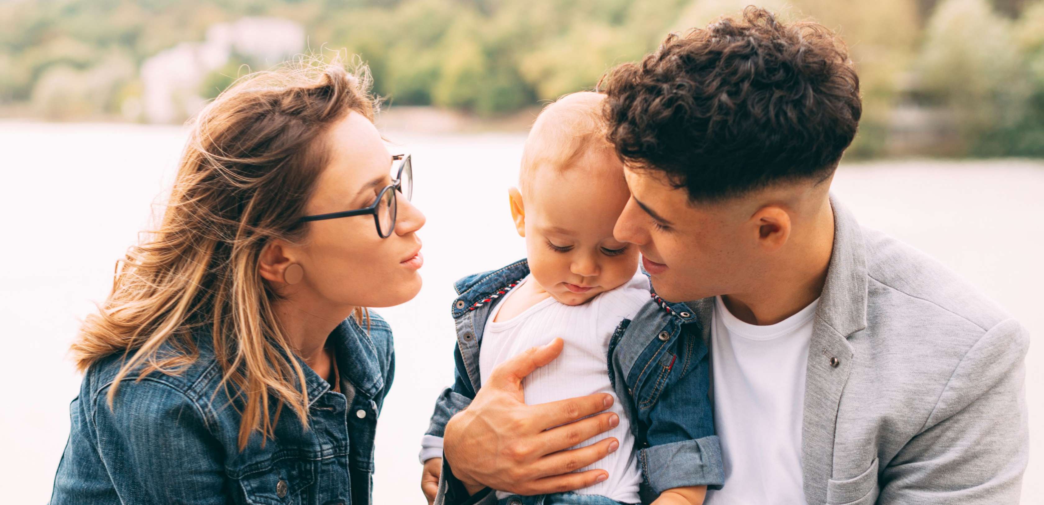 Allianz KinderPolice - Adoption: Eine Frau und Mann halten ein Kind in ihrer Mitte und schauen es liebevoll an.