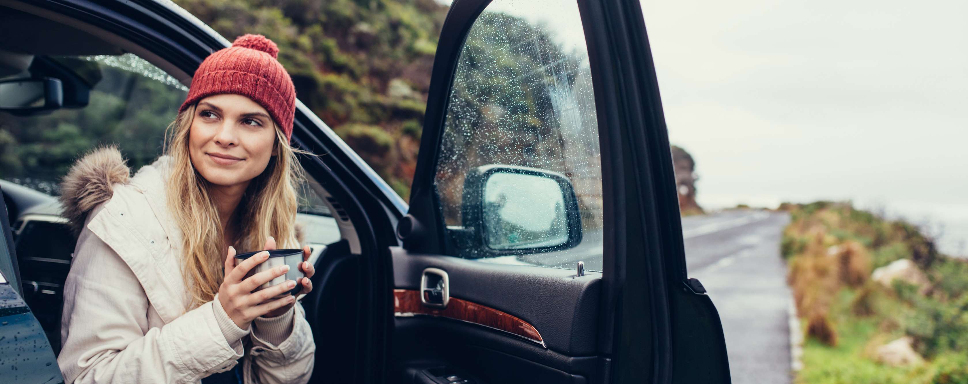 Allianz Private Altersvorsorge: Eine Frau sitzt im Auto am Straßenrand und trinkt einen Kaffee.