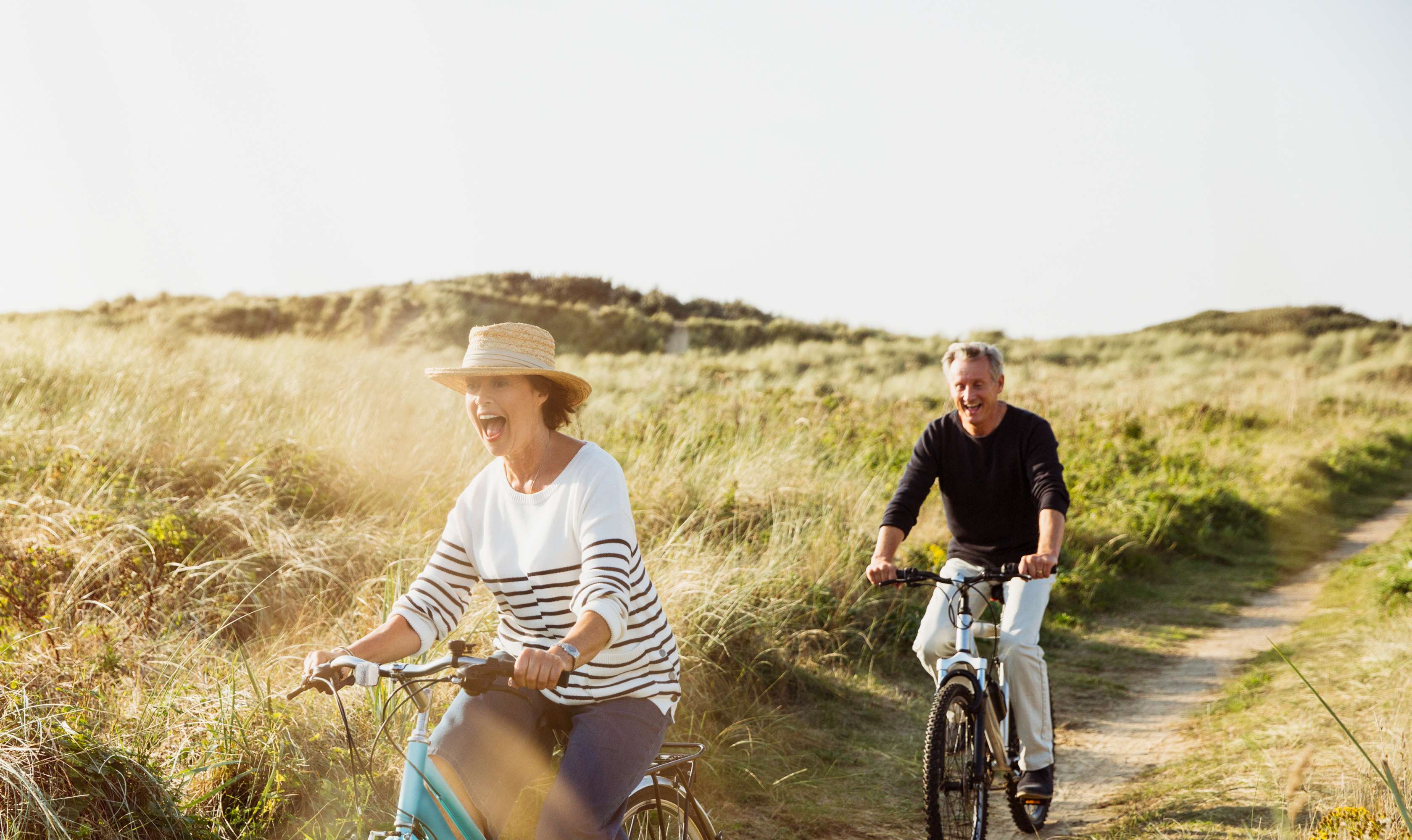Ein Senioren-Paar fährt gemeinsam mit dem Fahrrad durch Dünen.