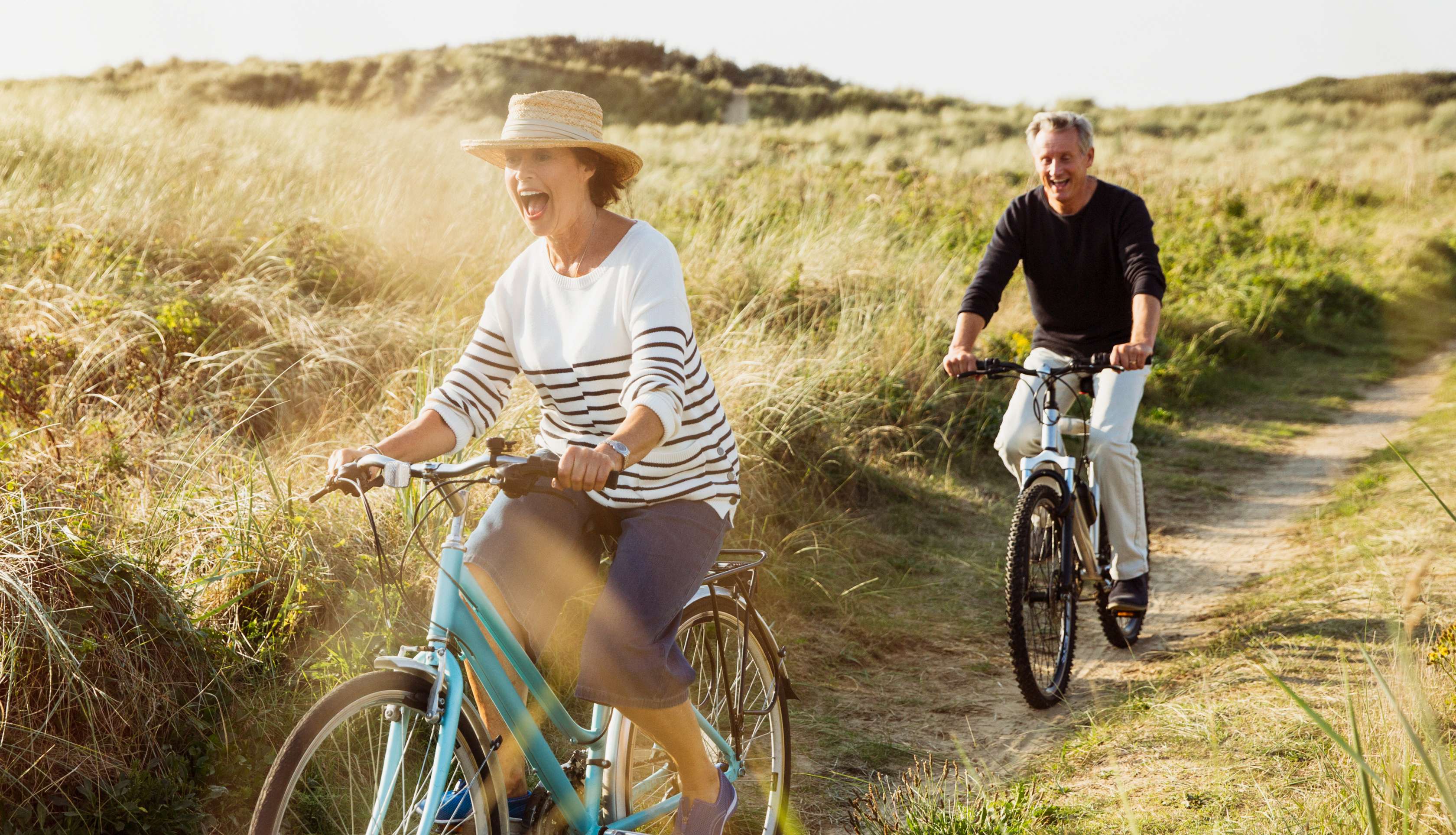 Allianz Private Rentenversicherung: Ein Senioren-Paar fährt gemeinsam mit dem Fahrrad durch Dünen.
