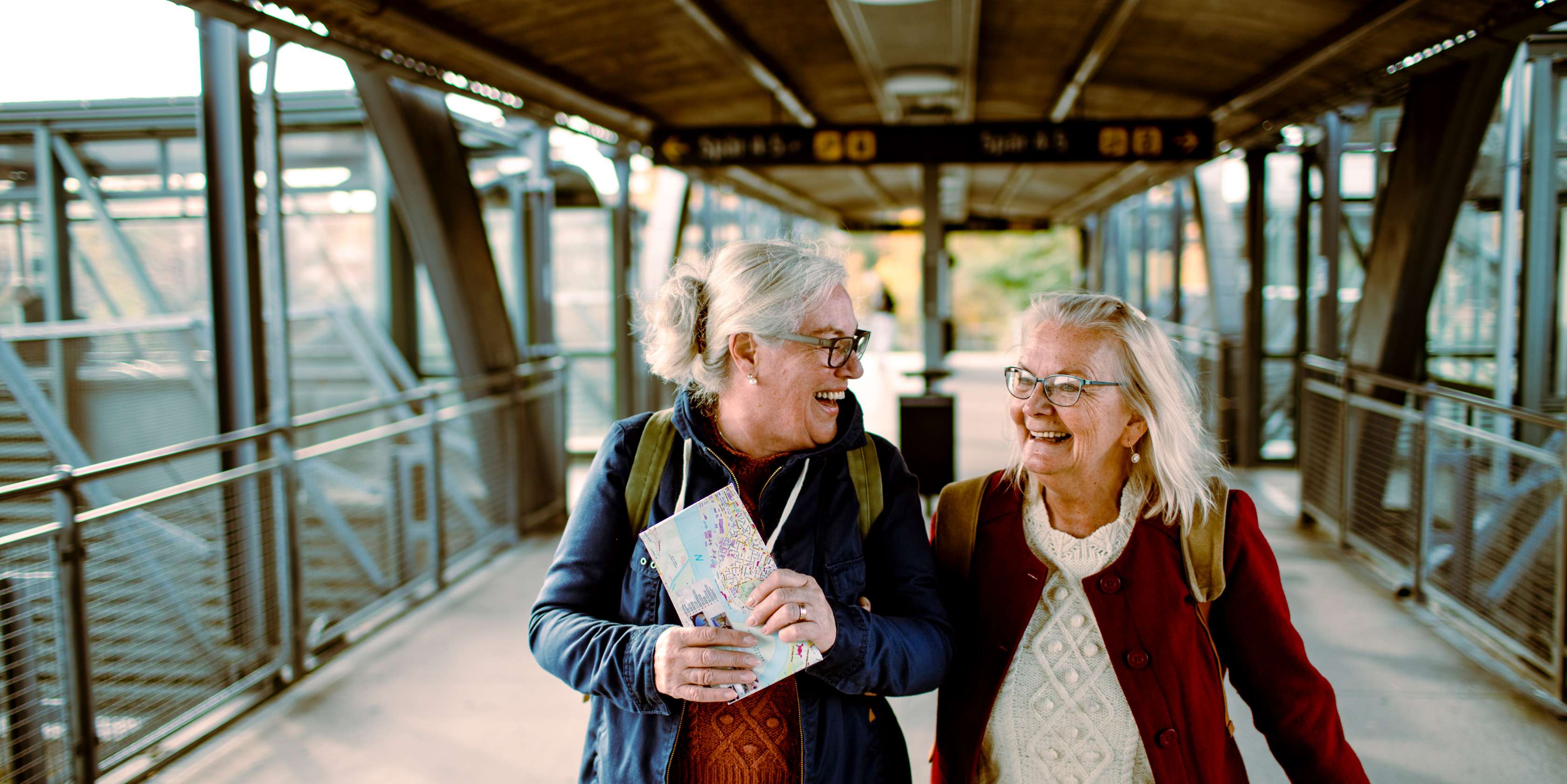 Allianz - Rente - Rente aufstocken: Zwei ältere Frauen auf einem Flughafen lachen sich an.